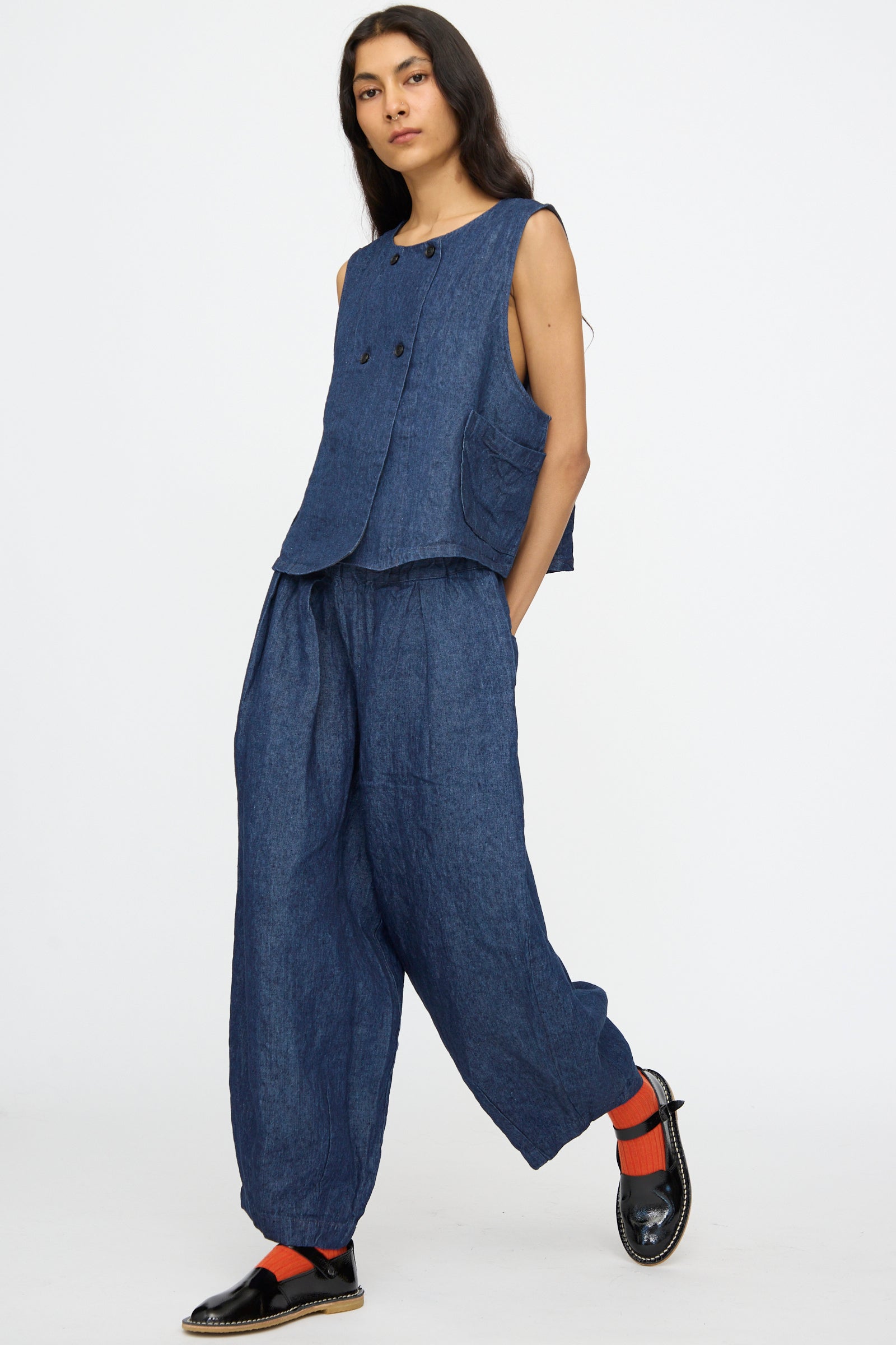 A person wears nest Robe's 10.oz Linen Denim Wide Tapered Trousers in Indigo Blue with a sleeveless blue top, black shoes, and red socks, standing against a plain white background.