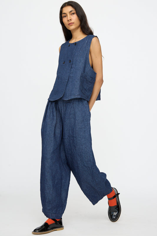 A person wears nest Robe's 10.oz Linen Denim Wide Tapered Trousers in Indigo Blue with a sleeveless blue top, black shoes, and red socks, standing against a plain white background.