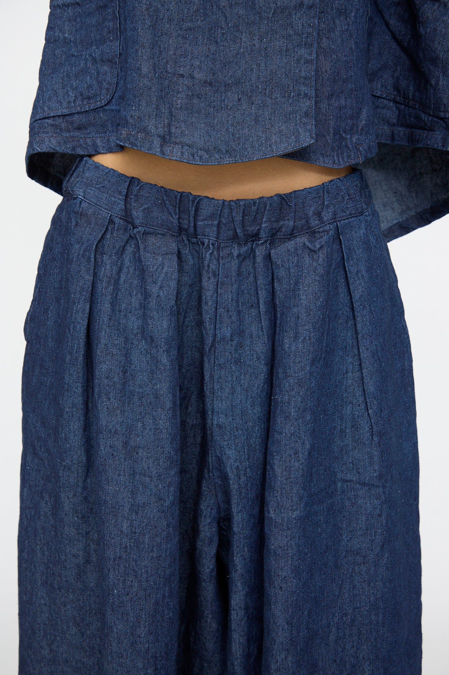 Close-up of a person wearing nest Robe’s 10.oz Linen Denim Wide Tapered Trousers in Indigo Blue, showing the waistband and styled with a matching cropped top.