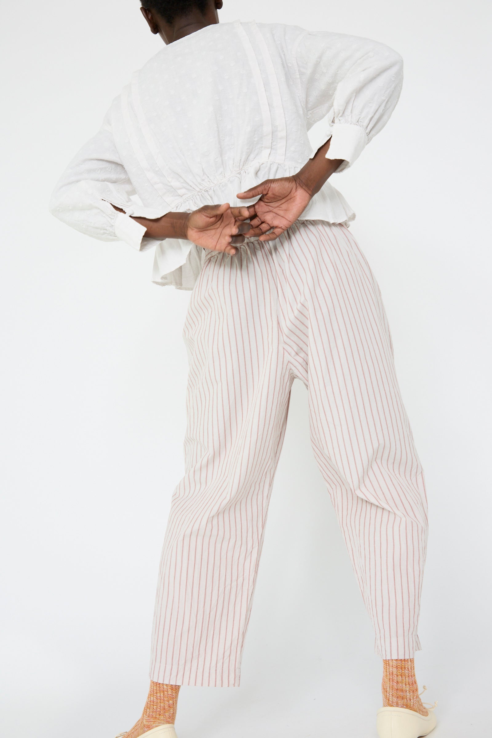 Person in a relaxed fit white blouse and nest Robe's Cotton Linen Easy Pants in Stripe facing away, with hand behind back.