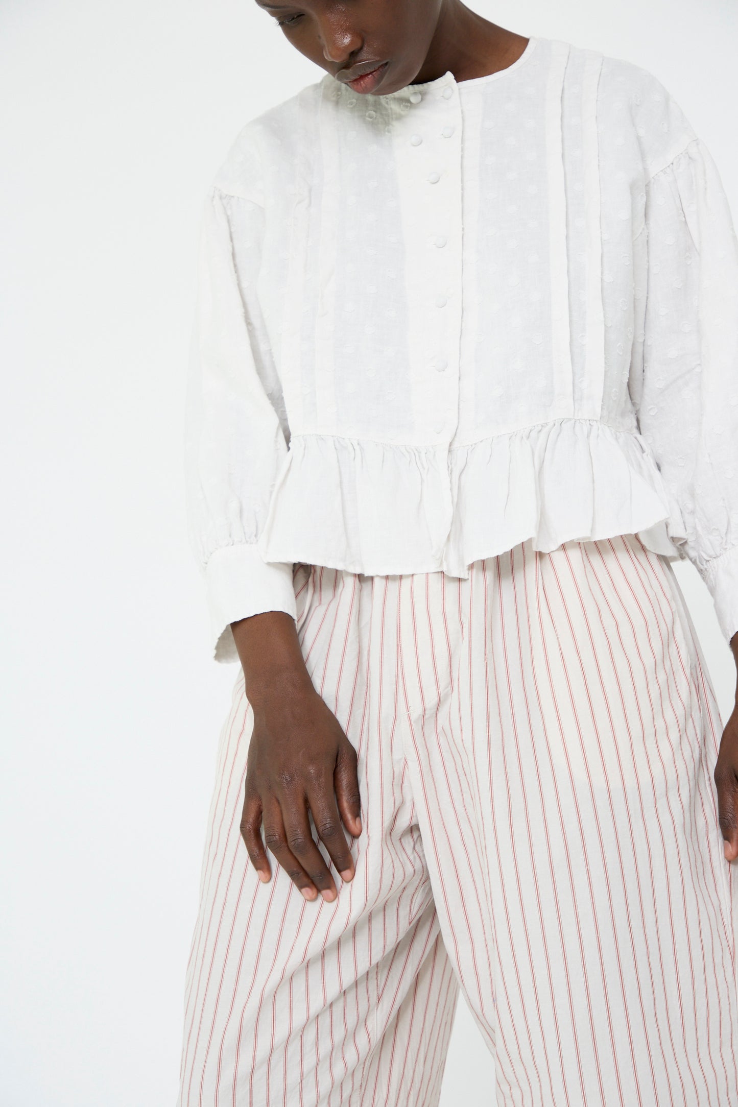 A person wearing a white button-up blouse with a ruffled hem and nest Robe's Cotton Linen Easy Pants in Stripe stands against a plain background.