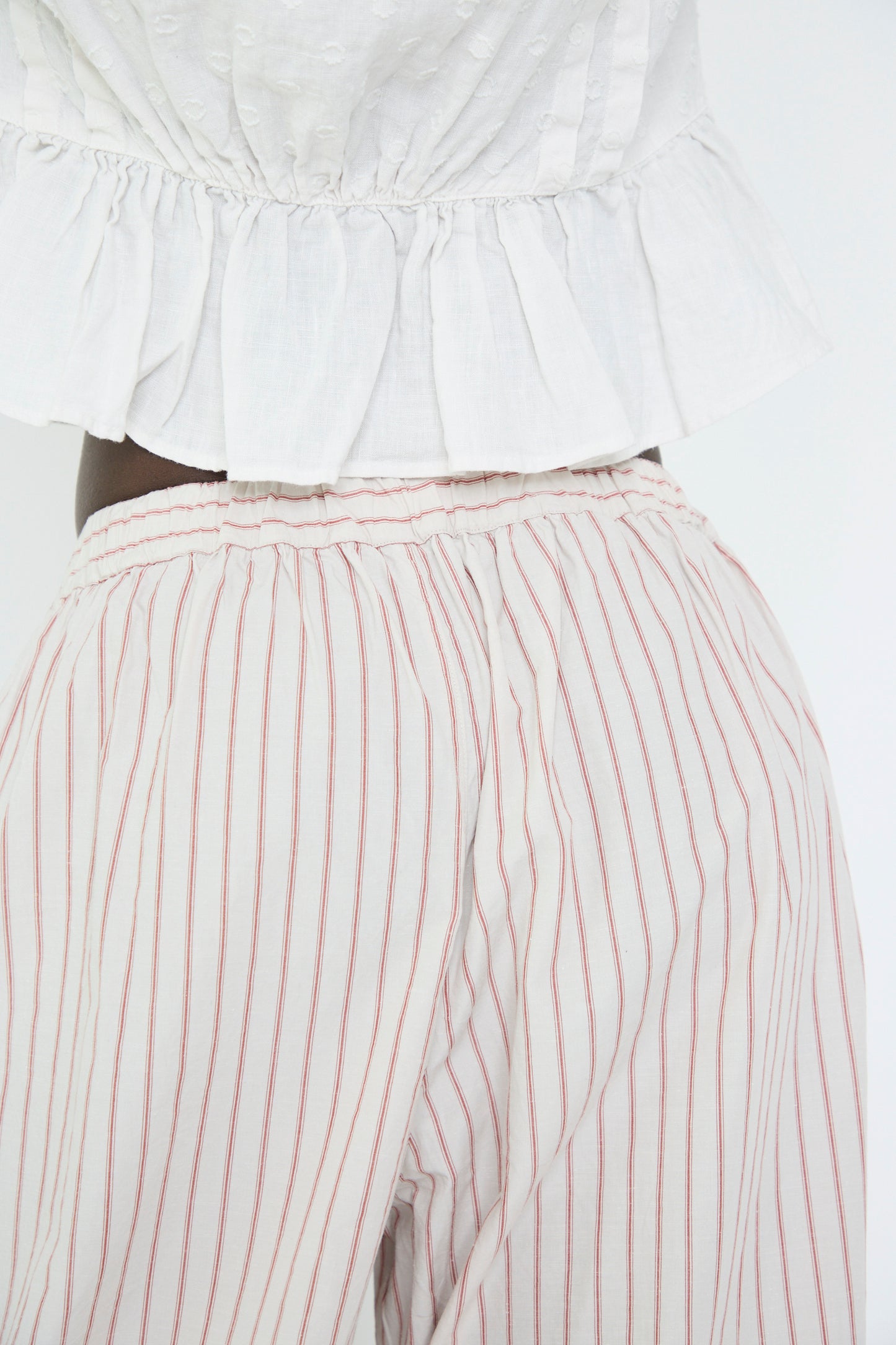 A close up of a woman wearing the nest Robe Cotton Linen Easy Pants in Stripe, stands with their back to the camera.