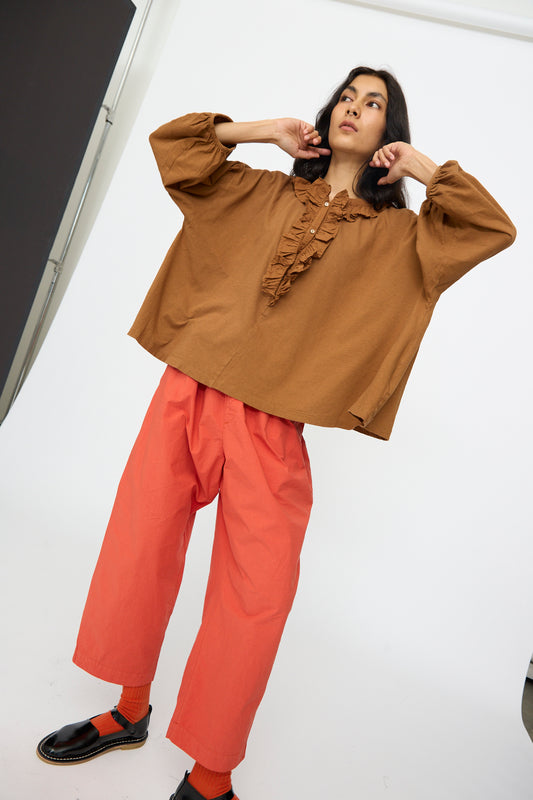 A person poses in the nest Robe Cotton Linen Frill Top in Brown, paired with loose coral pants, matching socks, and black shoes against a plain white background.