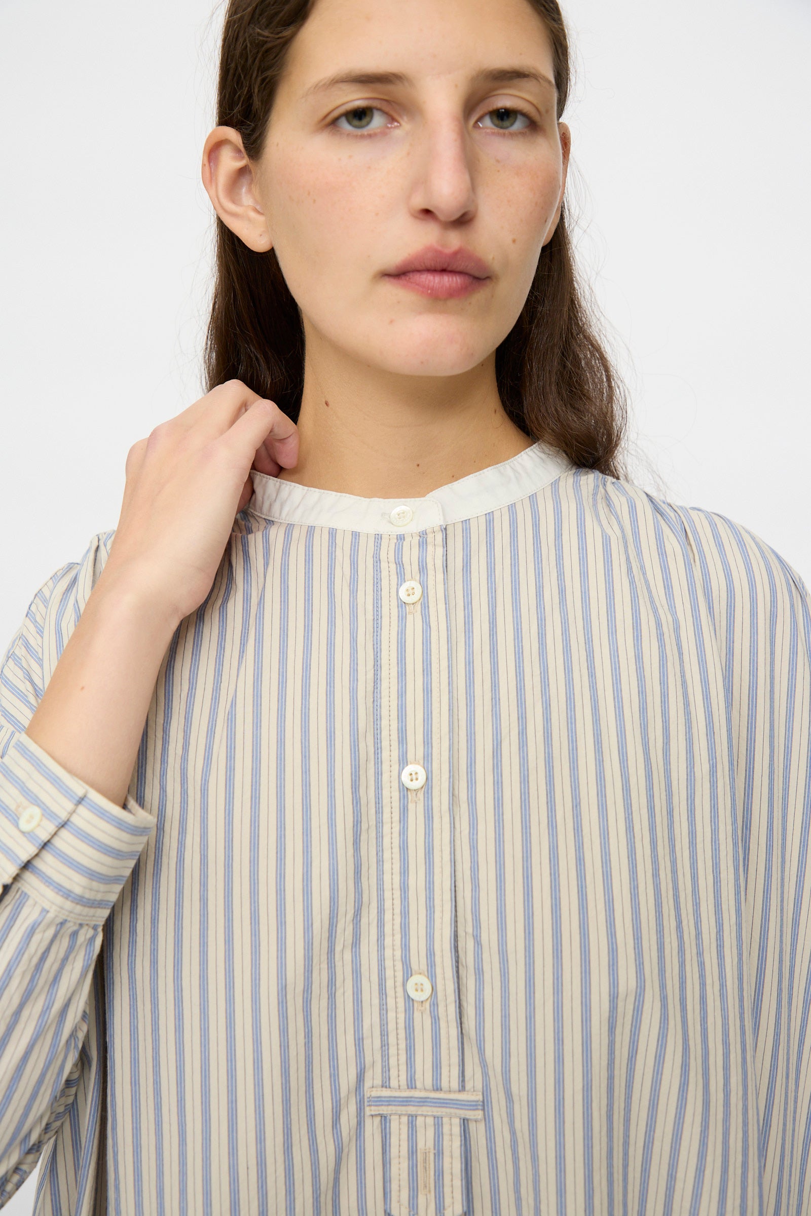 A person wears the nest Robe Cotton Pull-on Dress in Stripe, featuring loose, long sleeves and blue and beige stripes, made in Japan, standing against a plain light background.