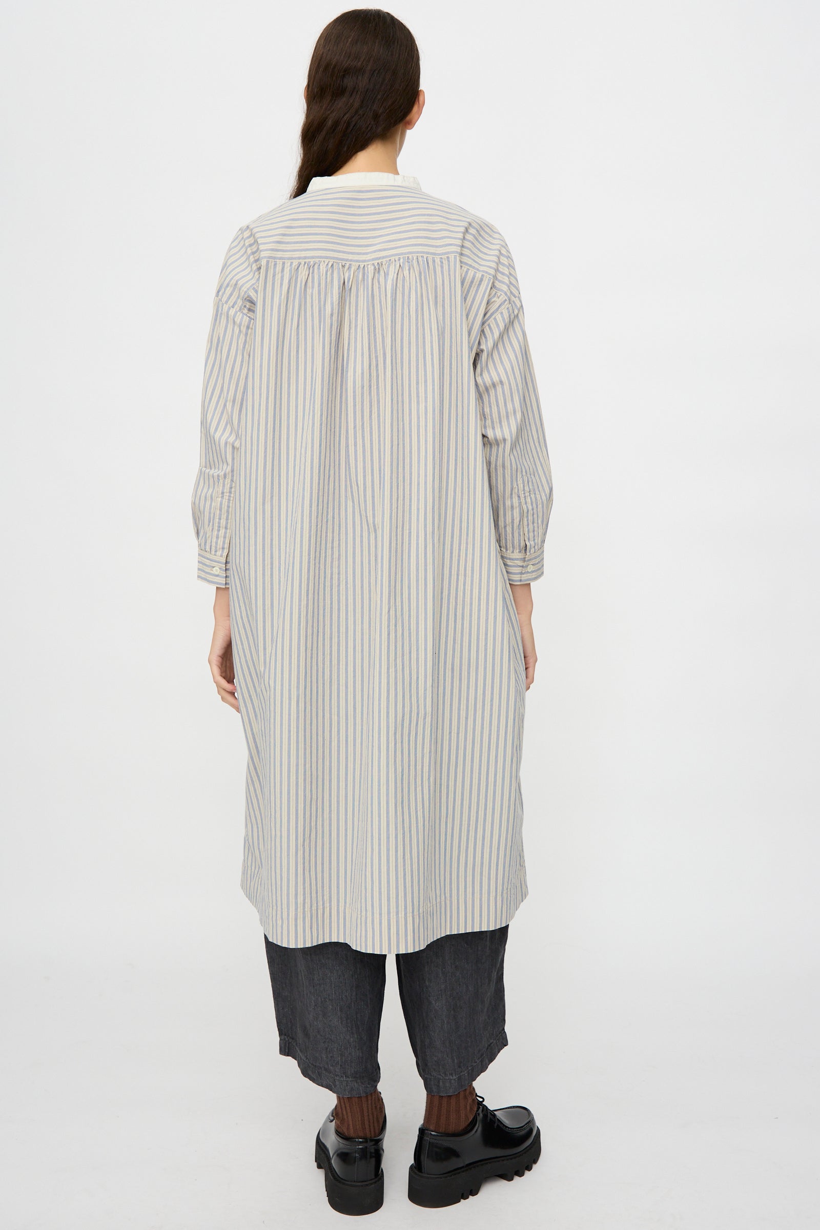 Person wearing the Cotton Pull-on Dress in Stripe by nest Robe, shown from the back with dark cropped pants and black shoes, standing against a plain white background.