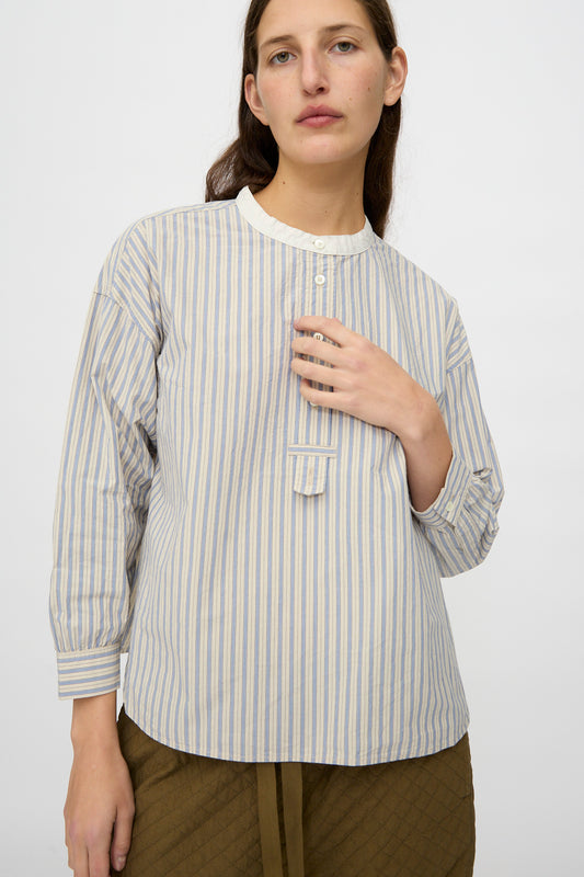 Wearing nest Robe's Cotton Pull-on Shirt in Stripe—a relaxed fit, blue and white striped cotton top with a white collar and button placket—paired with olive quilted pants, the person stands against a plain light background.