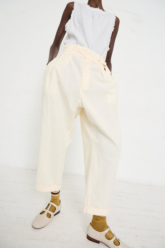 Person wearing a sleeveless white top and the Linen Cotton Blend Gurkah Pant in Off White by nest Robe, stands against a white background. They are also wearing beige-colored shoes and yellow socks.