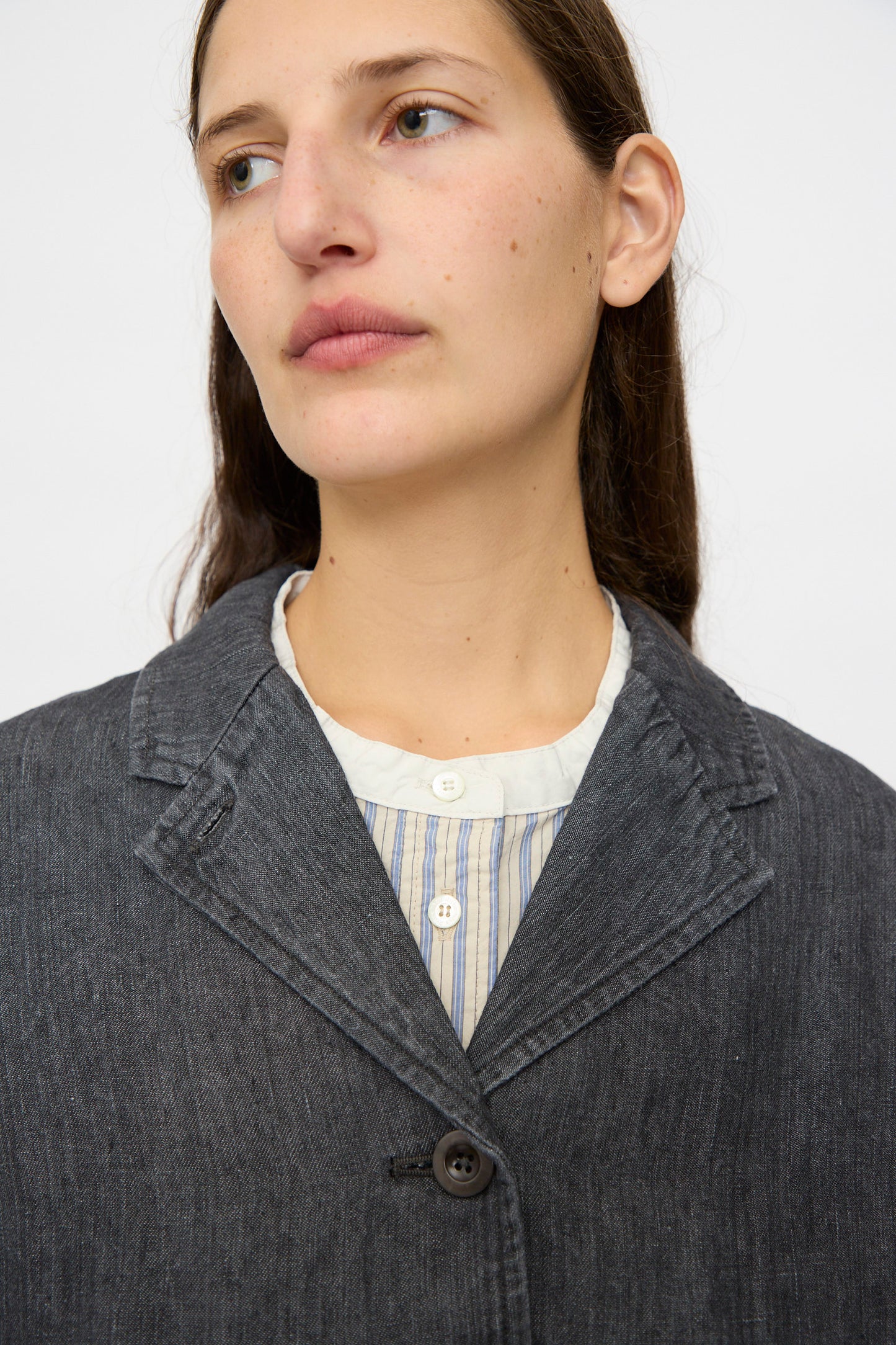 A person with long brown hair wears the nest Robe Linen Denim Cropped Jacket in Black over a white and blue striped shirt, looking slightly to the side against a plain background.
