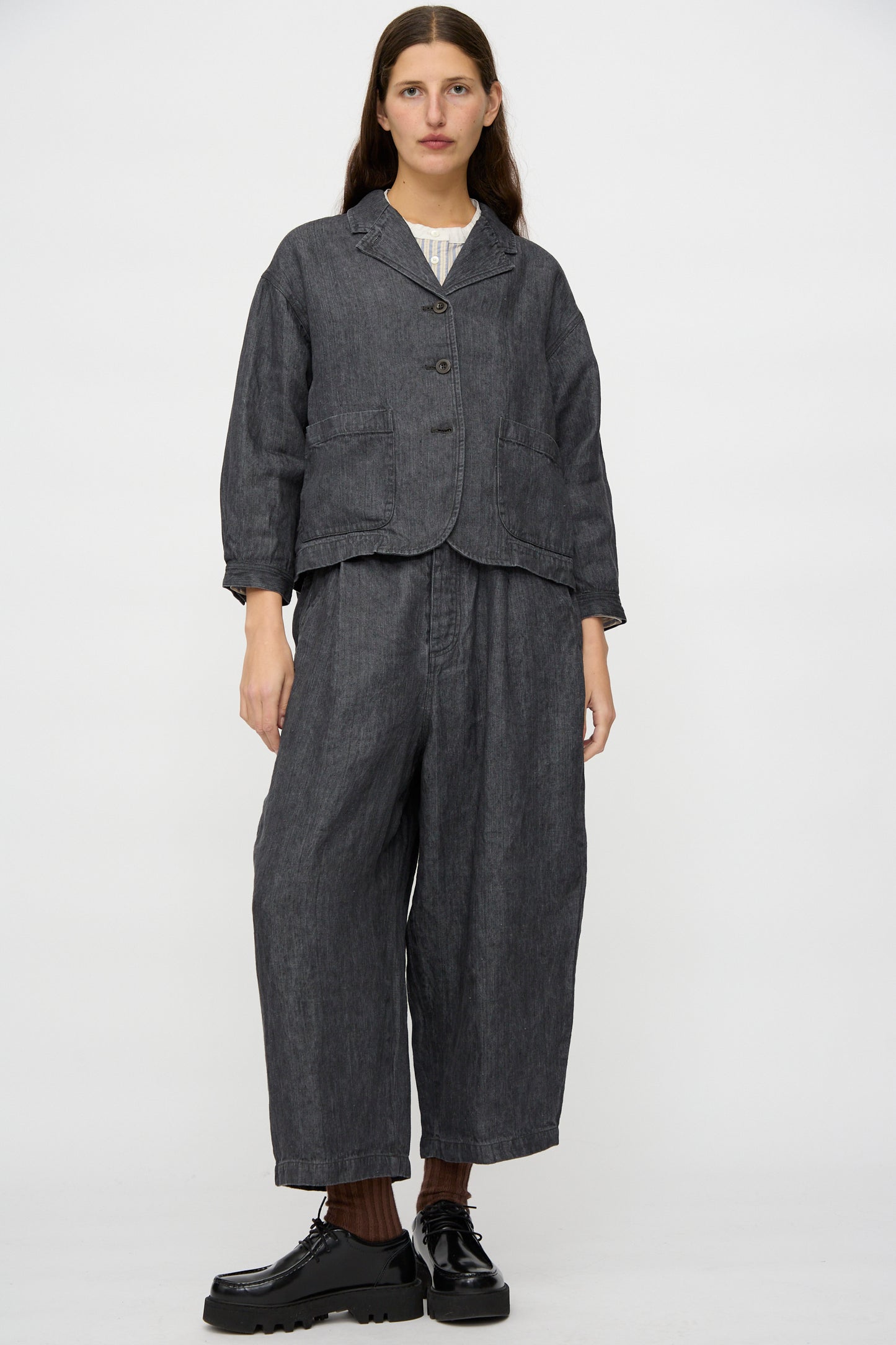 A person faces forward against a white background, wearing nest Robe's Linen Denim Wide Pants in Black paired with a loose black jacket and black platform shoes.
