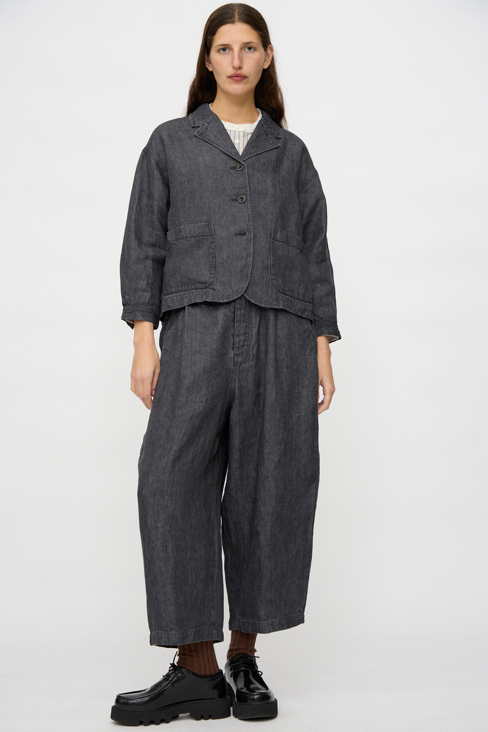 A person faces forward against a white background, wearing nest Robe's Linen Denim Wide Pants in Black paired with a loose black jacket and black platform shoes.
