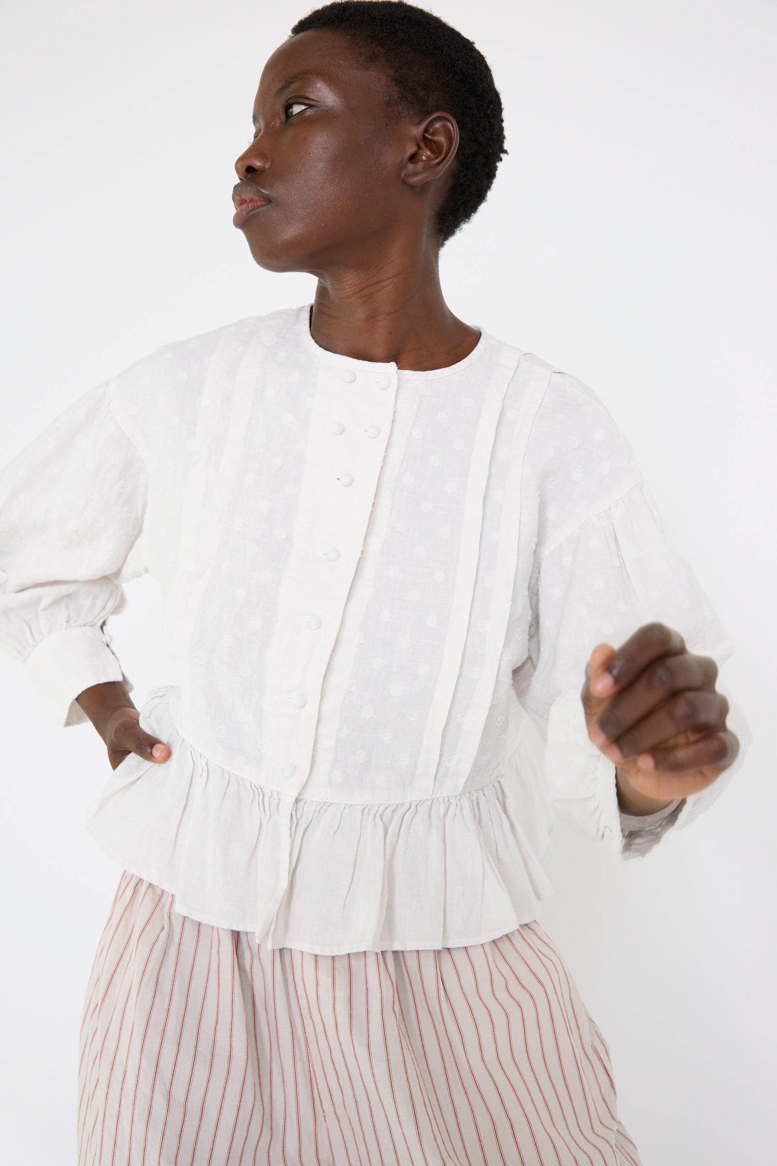 A woman wears the Linen Dot Jacquard Blouse in Off White by nest Robe with a striped skirt and stands against a plain white background.