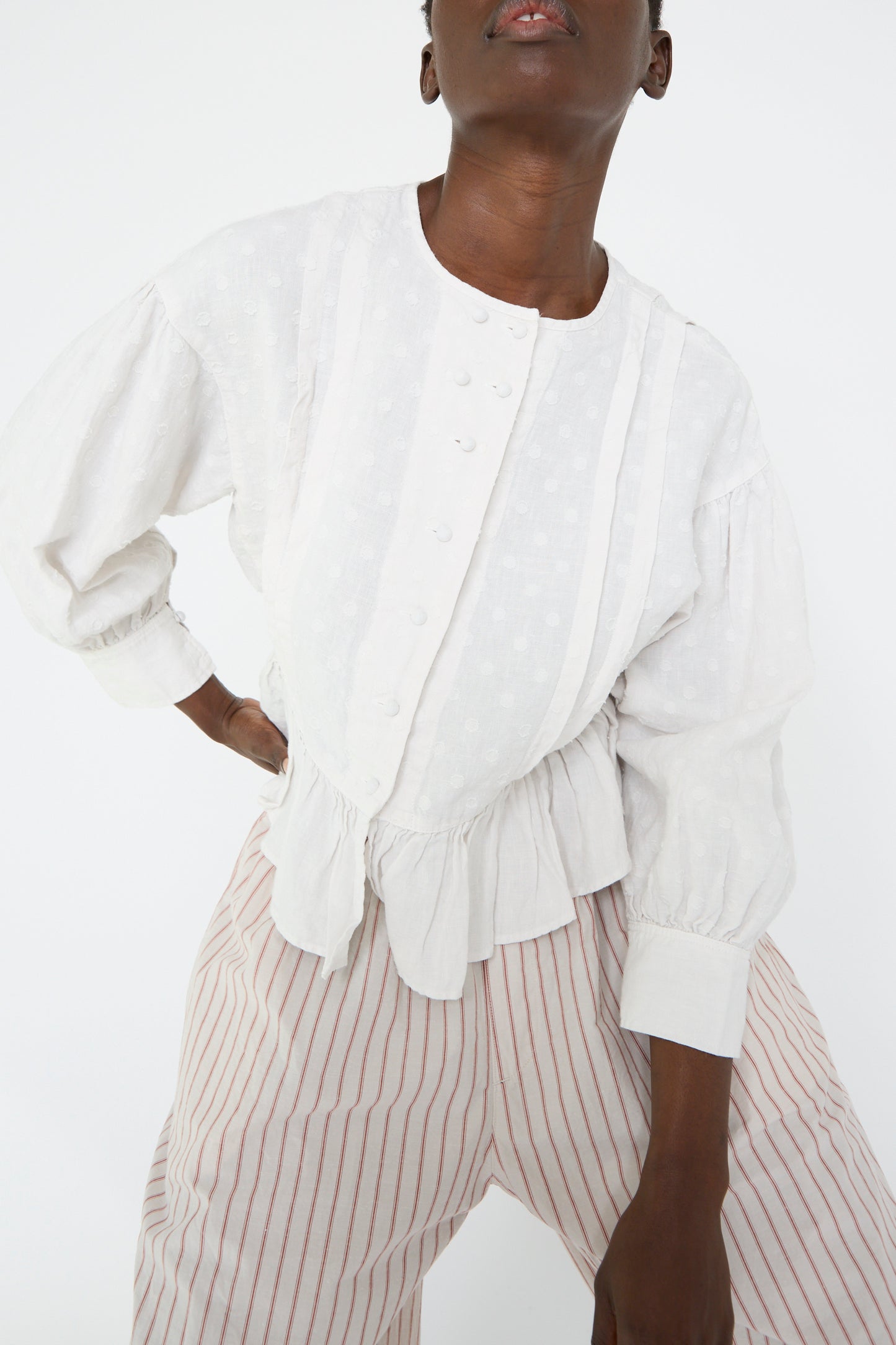 A woman wears the Linen Dot Jacquard Blouse in Off White by nest Robe with striped pants while posing against a plain background.