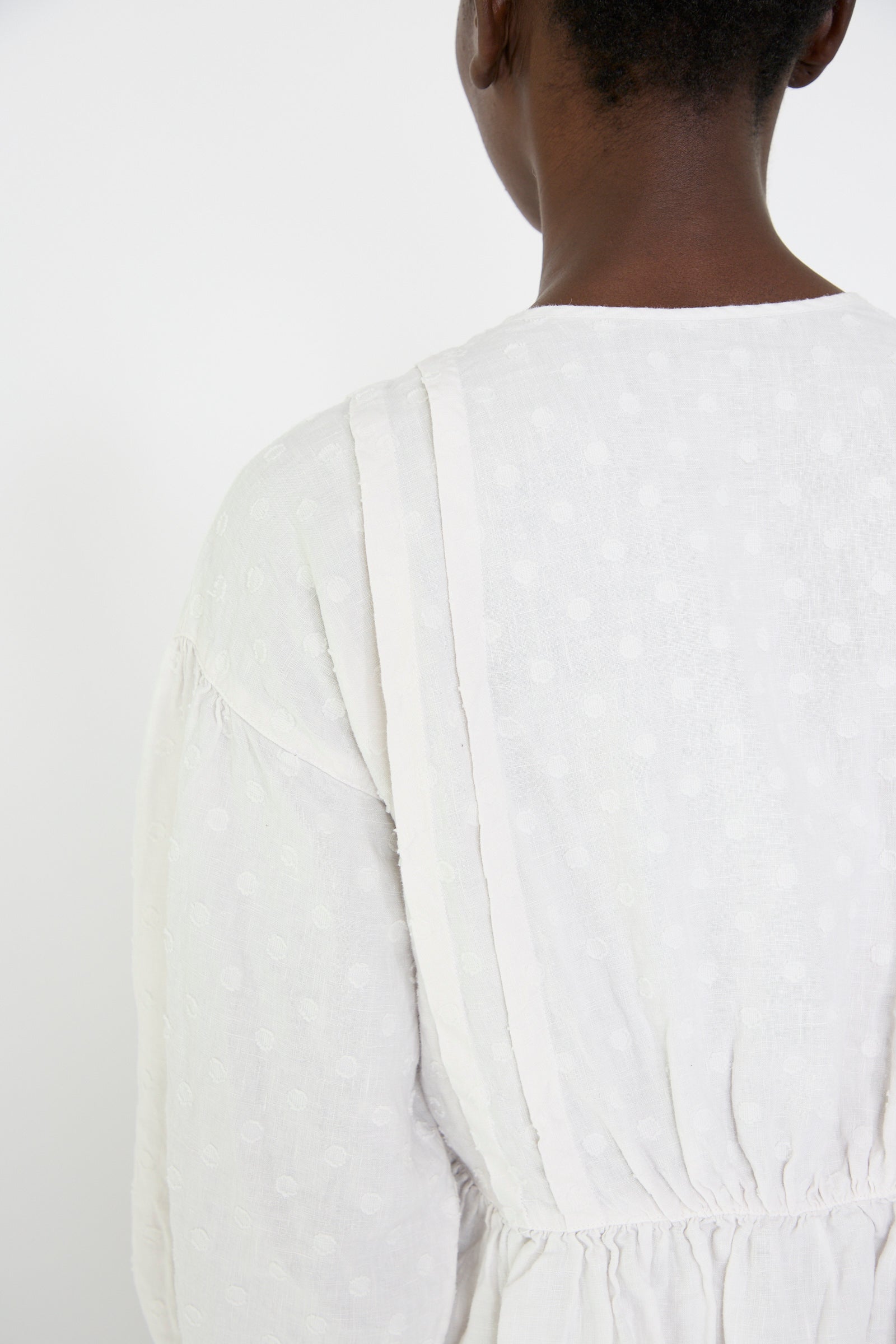 Rear view of a person wearing the Linen Dot Jacquard Blouse in Off White by nest Robe, standing against a plain white background.