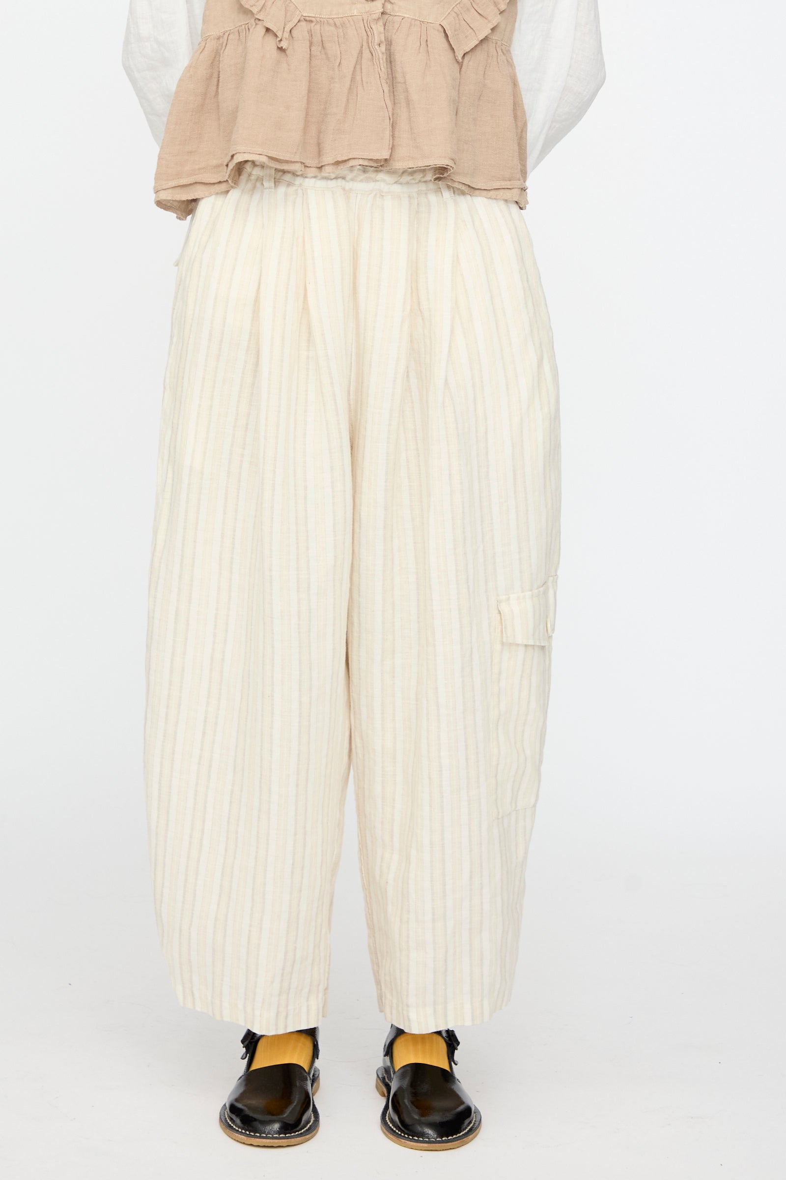 A person wears nest Robe's Linen Easy Pants in Natural Stripe with a beige top, yellow socks, and black sandals, shown from shoulders down against a white background.