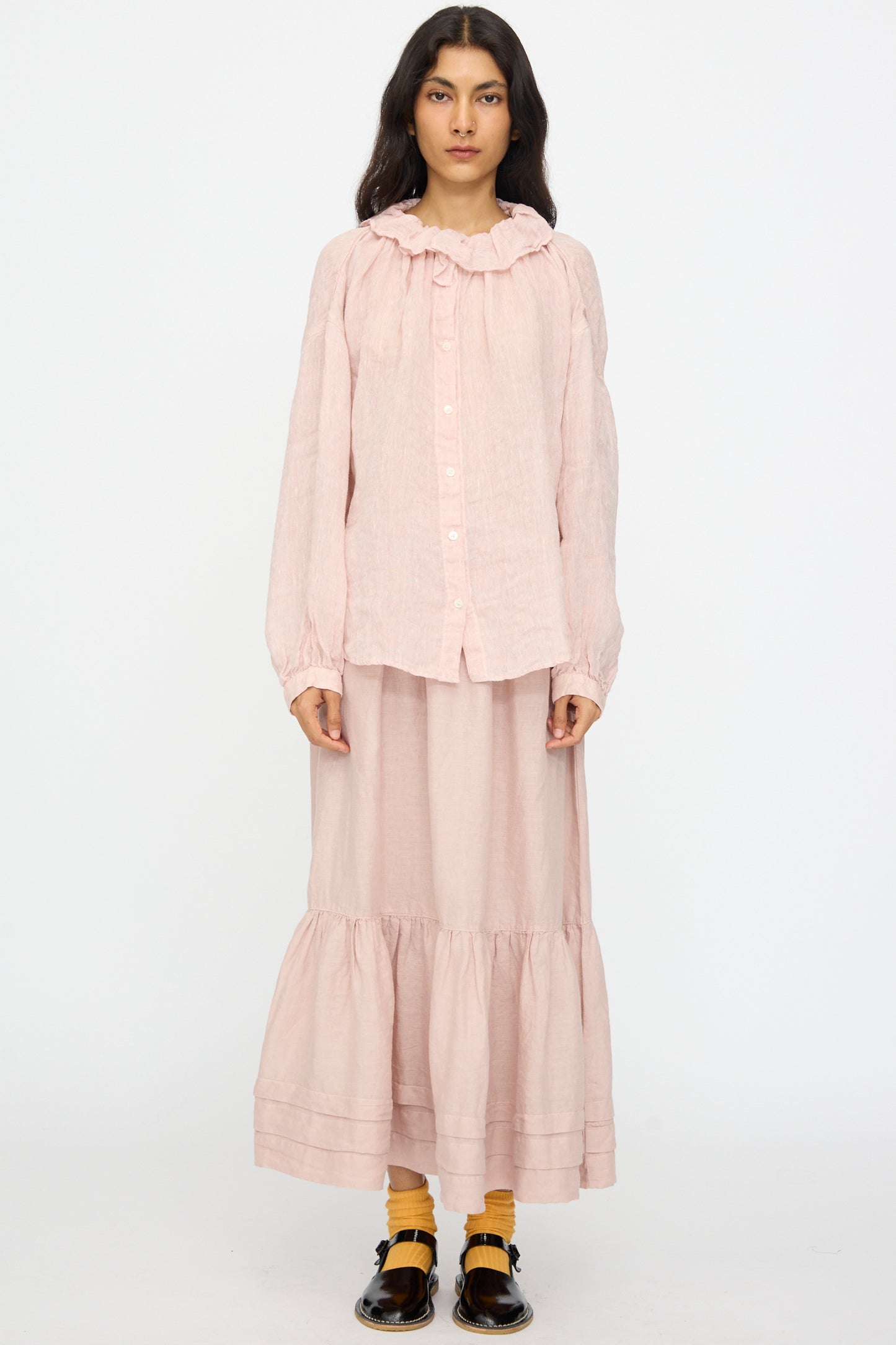 A person stands facing forward wearing the nest Robe Linen Gauze Frill Blouse in Light Peach, a matching tiered midi skirt, yellow socks, and black shoes.