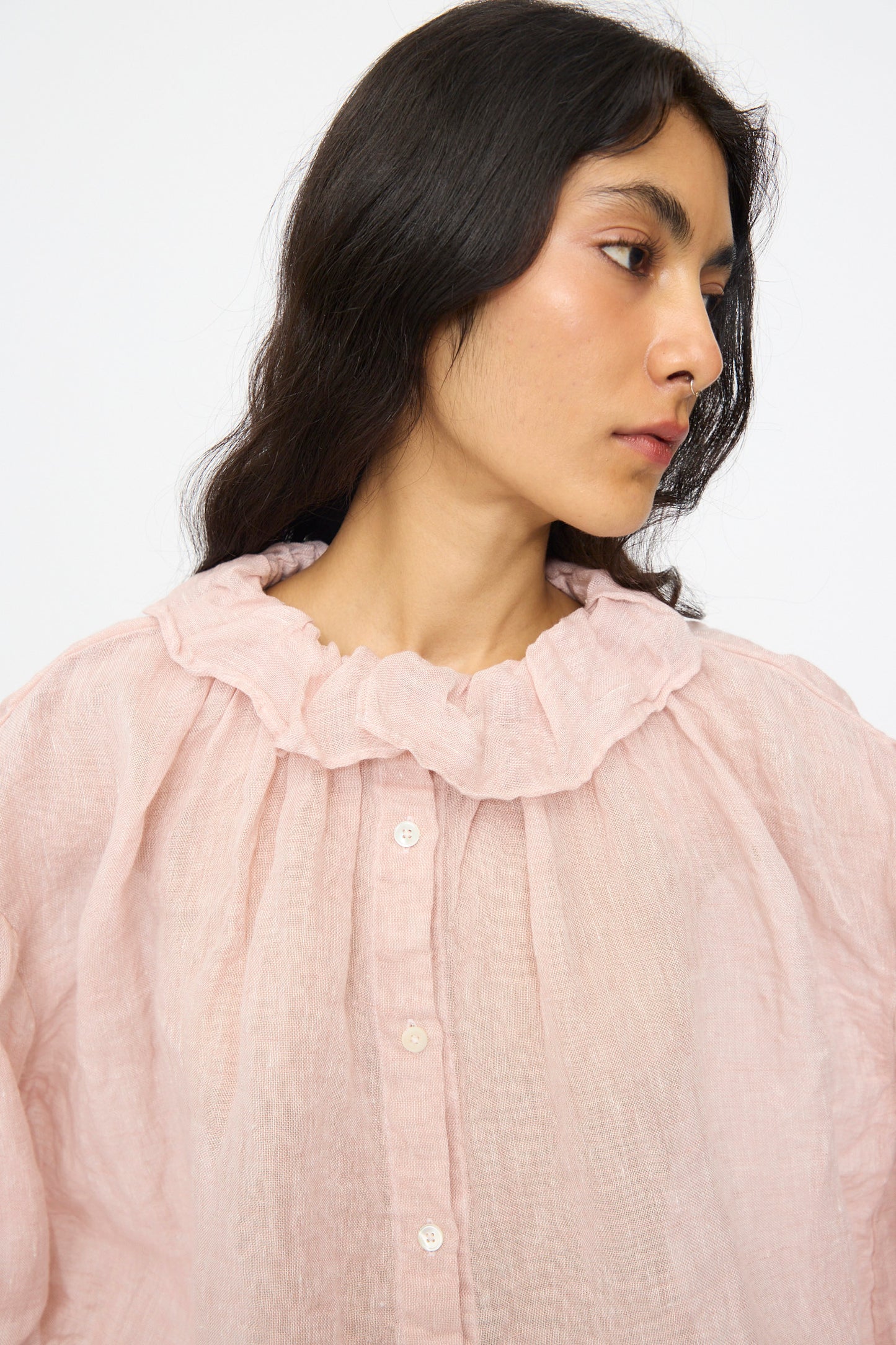 A person with long dark hair wears the nest Robe Linen Gauze Frill Blouse in Light Peach, featuring long sleeves and a ruffle collar, while looking to the side against a plain background.