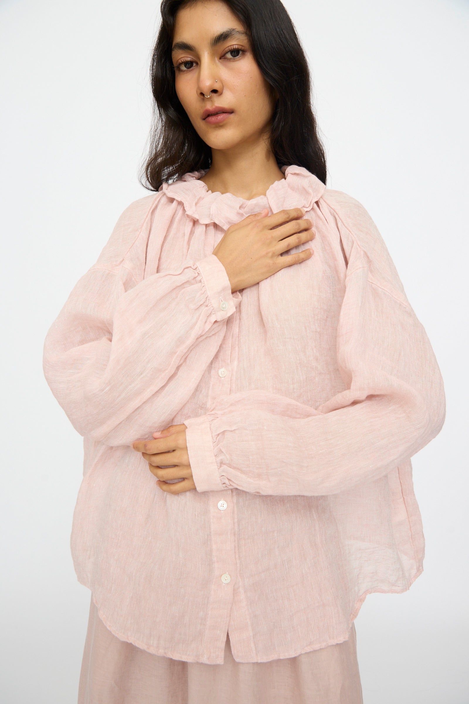 A person models the nest Robe Linen Gauze Frill Blouse in Light Peach, a loose-fit linen top with long sleeves and a ruffle collar, standing against a plain background with one hand on their chest and one resting on their torso.