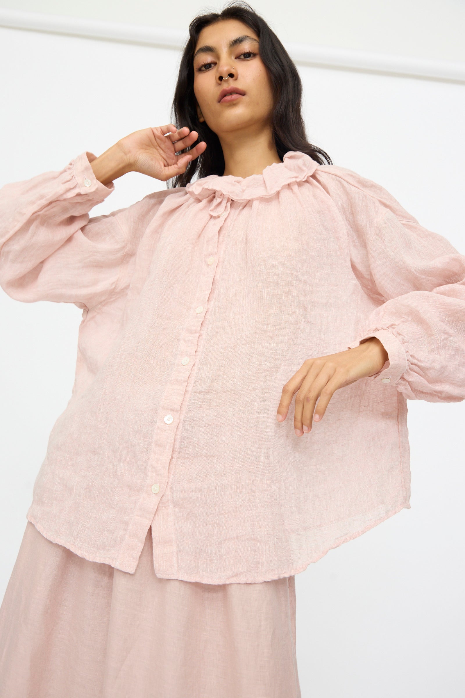 A woman wears the nest Robe Linen Gauze Frill Blouse in Light Peach, featuring long sleeves and a ruffle collar, against a plain white background.