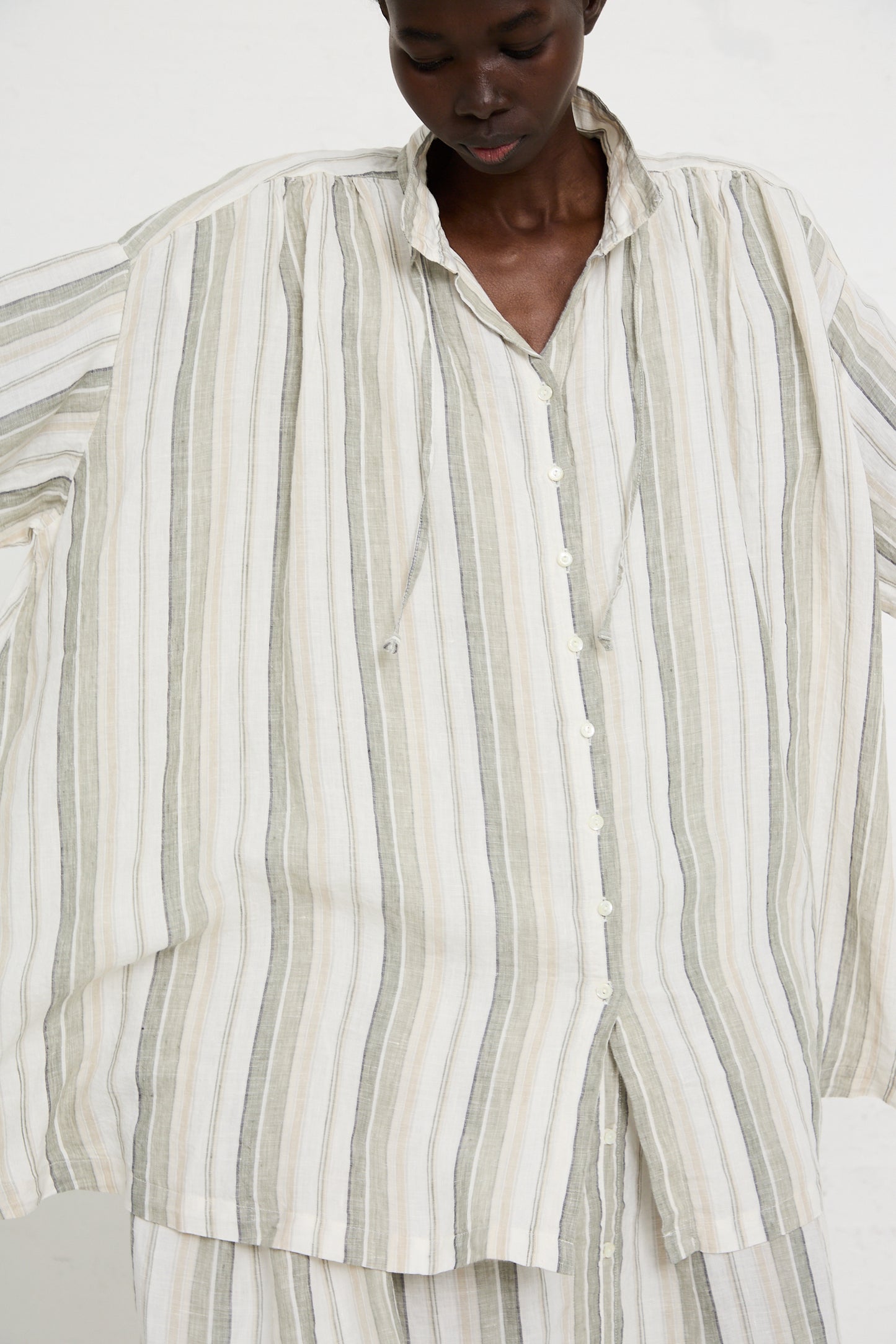 Person wearing an oversized, striped Linen Long Oversized Shirt in Stripe by nest Robe with vertical green and beige stripes, looking down.