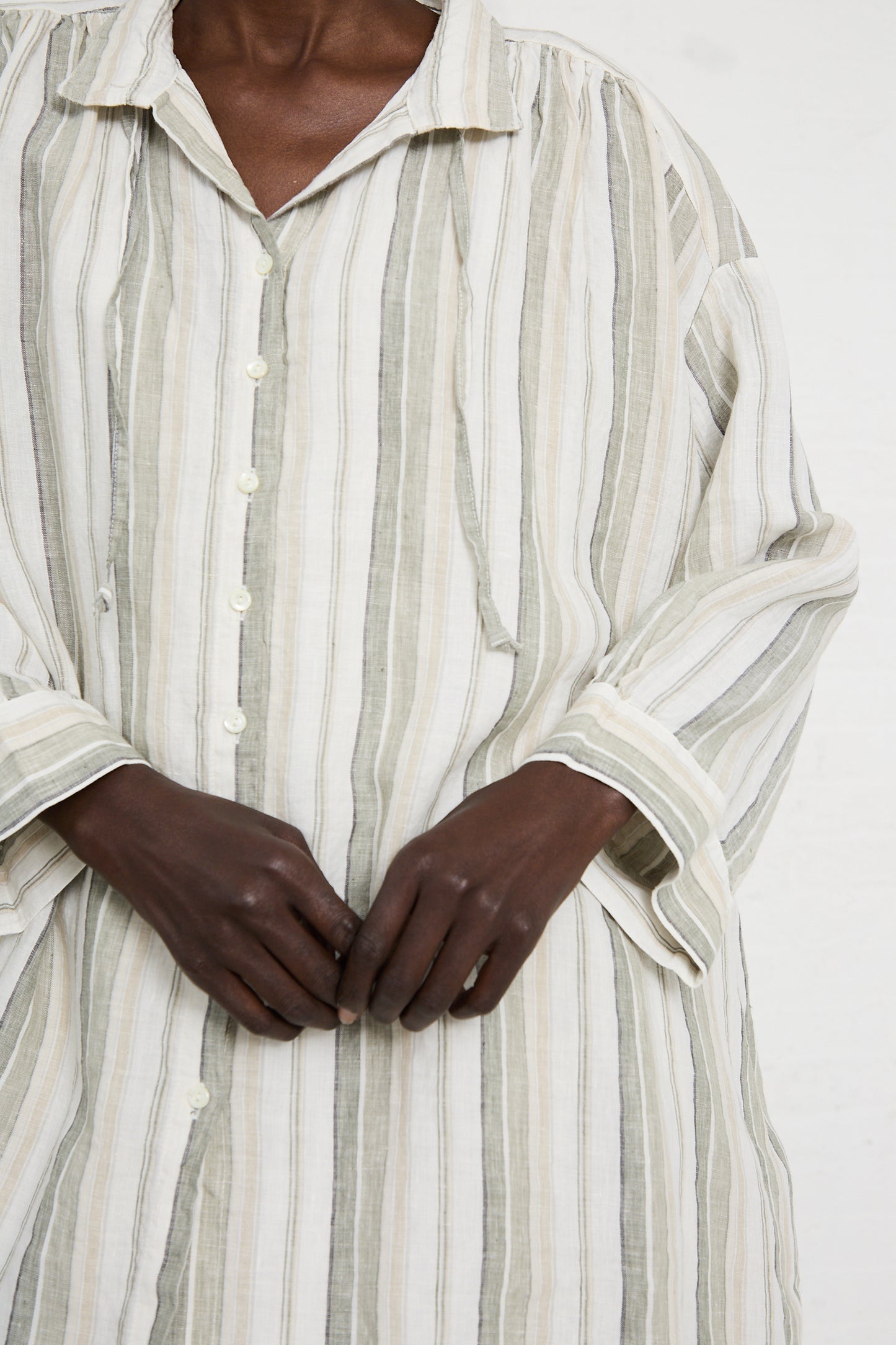A person is wearing a nest Robe Linen Long Oversized Shirt in Stripe, holding their hands together.
