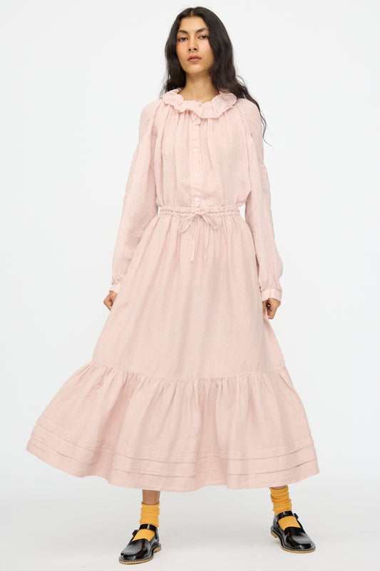 A woman in a nest Robe Linen Natural Dyed Pleated Gathered Skirt in Pink, yellow socks, and black sandals stands against a plain white background.