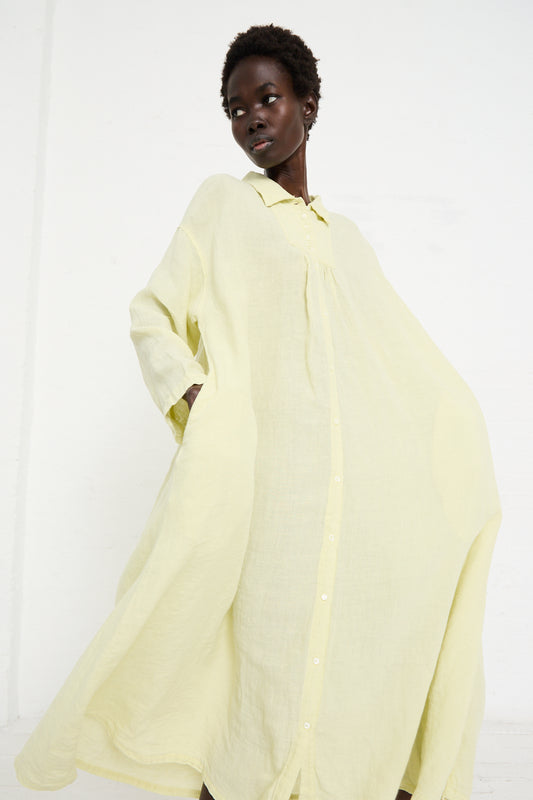 Person in a flowing, pale yellow Linen Omi-Zarashi Brocante Shirt Dress in Lemon by nest Robe poses against a plain white background.