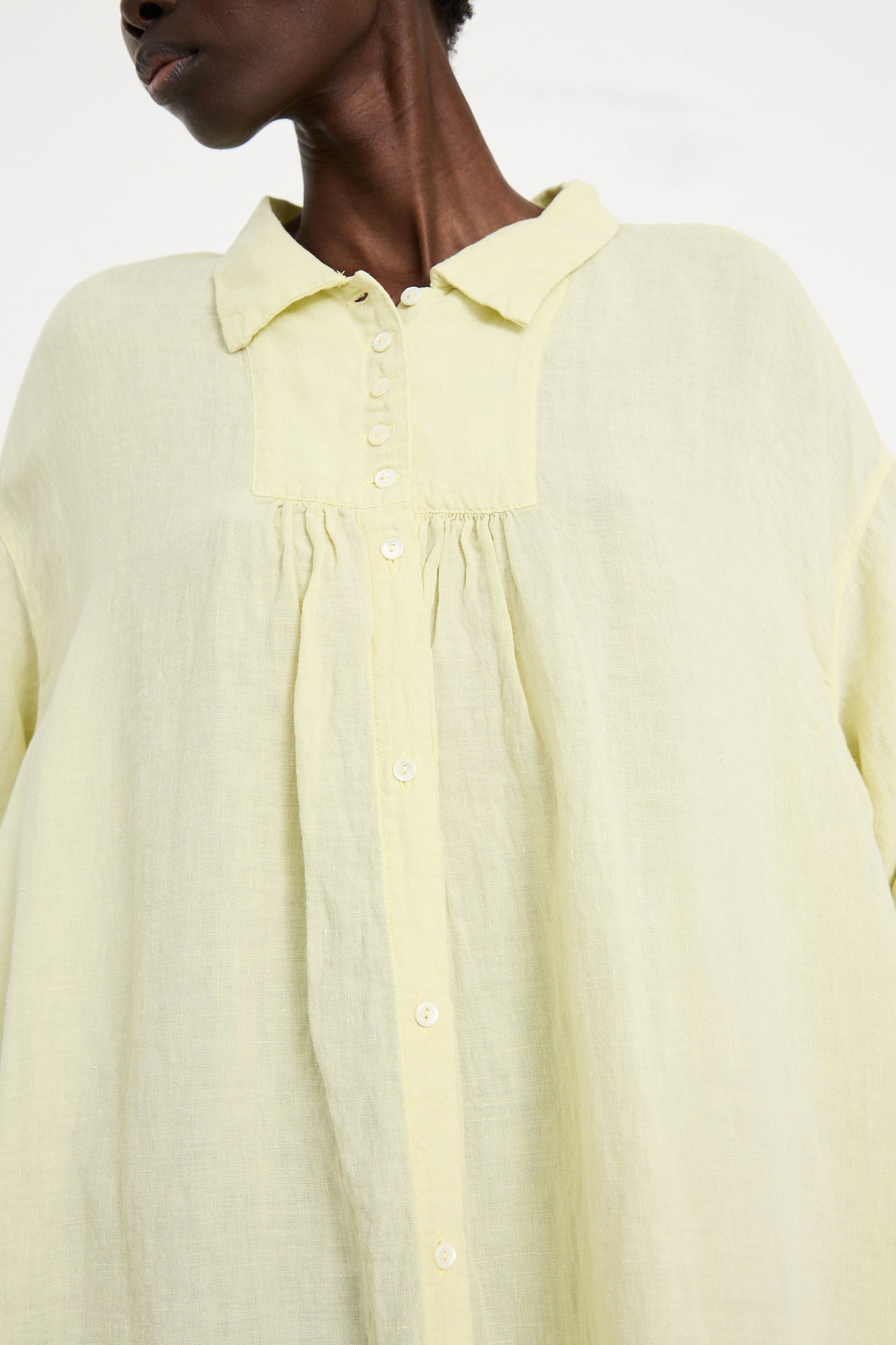 Close-up of a person wearing a Linen Omi-Zarashi Shirt Dress in Lemon by nest Robe with a collar and gathered details below the yoke. The focus is on the shirt's design.