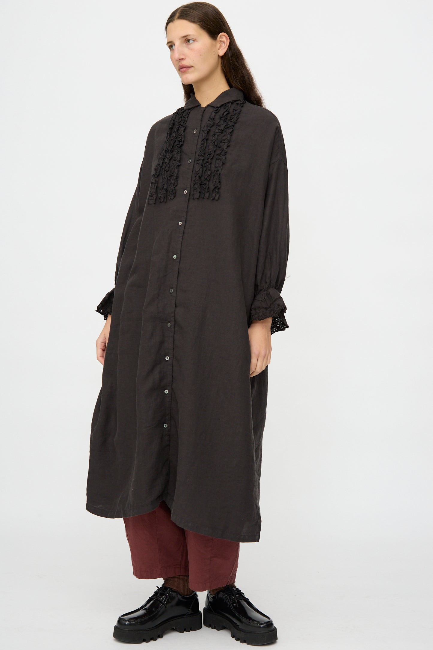 A person wears the nest Robe Linen Scallop Lace Dress in Ink Black with red pants and black platform shoes, standing against a plain white background.