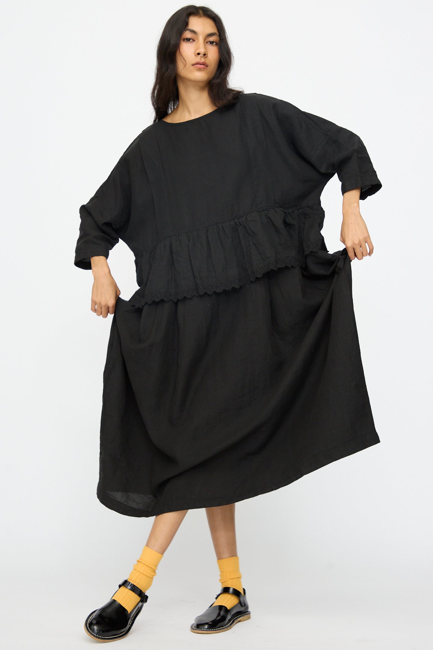 A person wears the nest Robe Linen Scallop Lace Two-Way Peplum Dress in Black, paired with yellow socks and black shoes, standing against a white background. The dress offers effortless Japanese style and comfort.