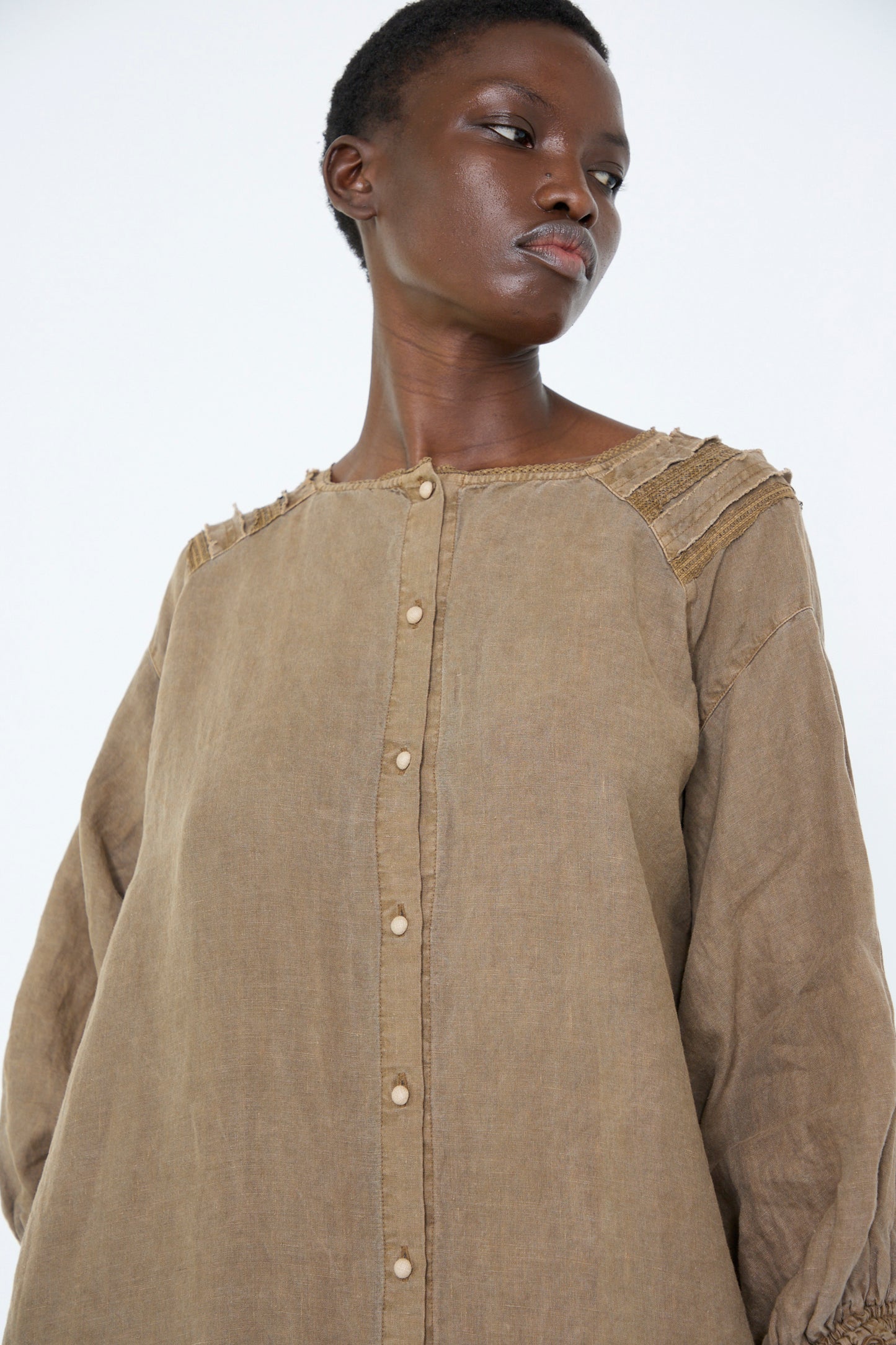 A woman wearing the Natural Dyed Linen Cotton Lace Dress in Camel from nest Robe, gazes to the side against a plain background.