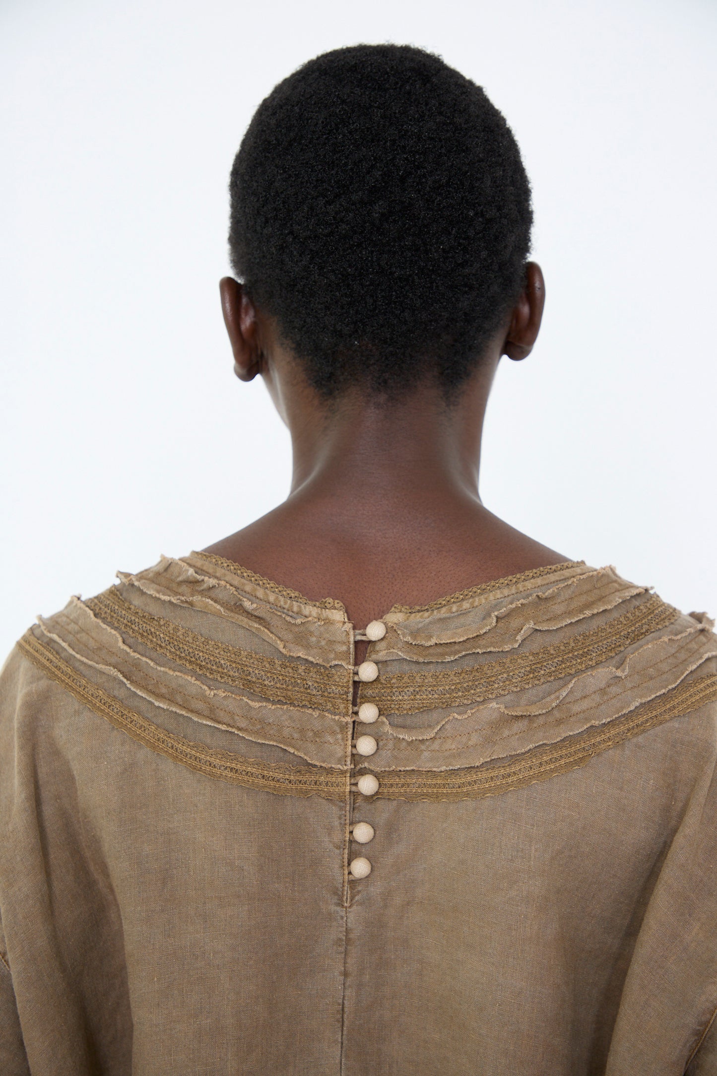 The back view of a woman wearing the Natural Dyed Linen Cotton Lace Dress in Camel by nest Robe, set against a simple background.