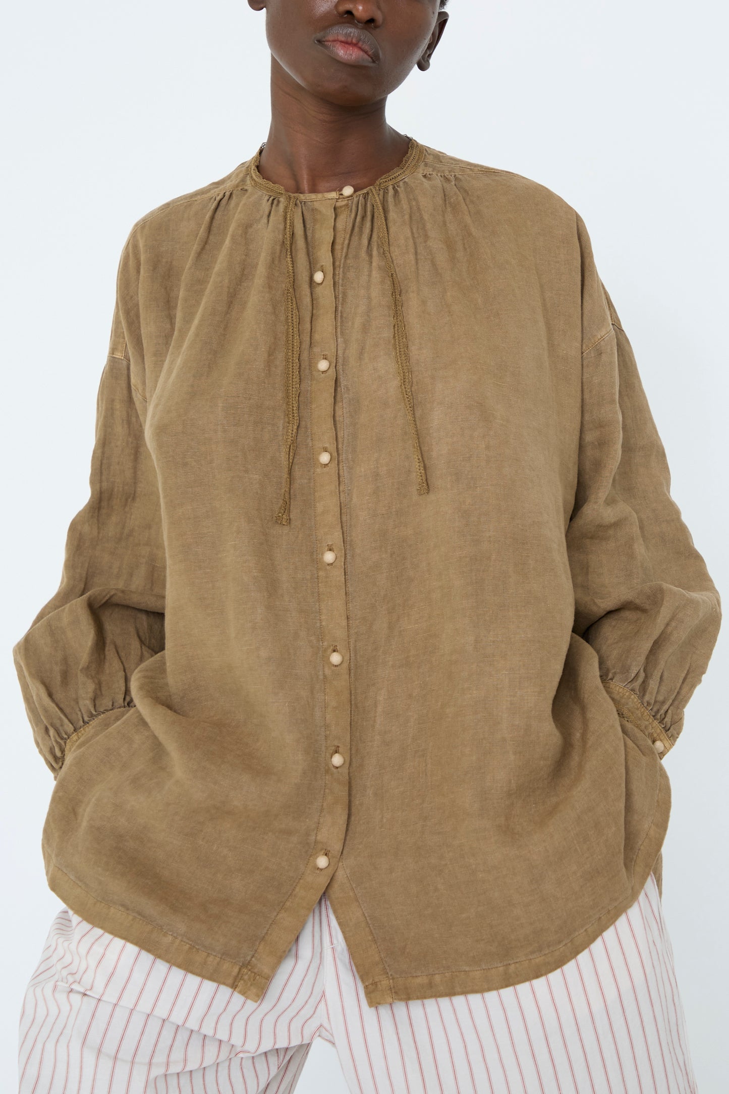 A woman wearing the Natural Dyed Linen Cotton Lace Shirt in Camel by nest Robe, featuring an oversized fit and gathered sleeves with her hands in her pockets.