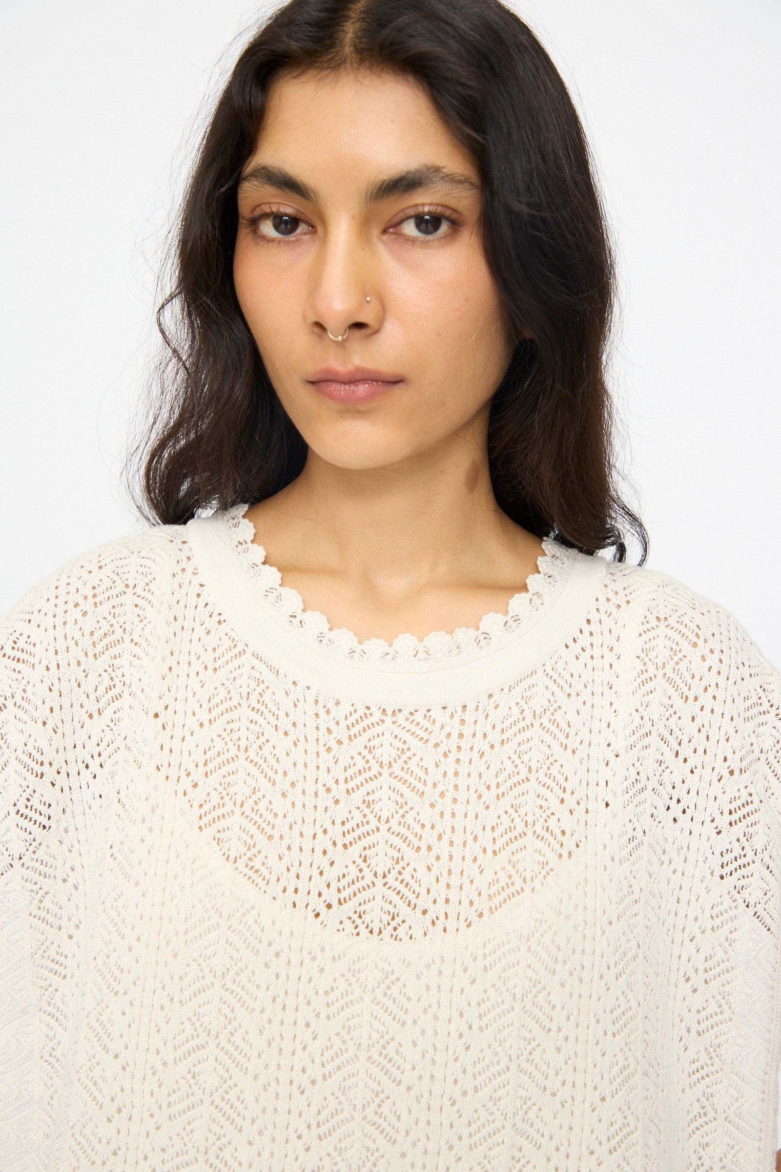 Woman with long dark hair wears the Openwork Lace Knit Vest in Off White by nest Robe, featuring a crocheted knit and scalloped neckline, looking directly at the camera against a plain background.
