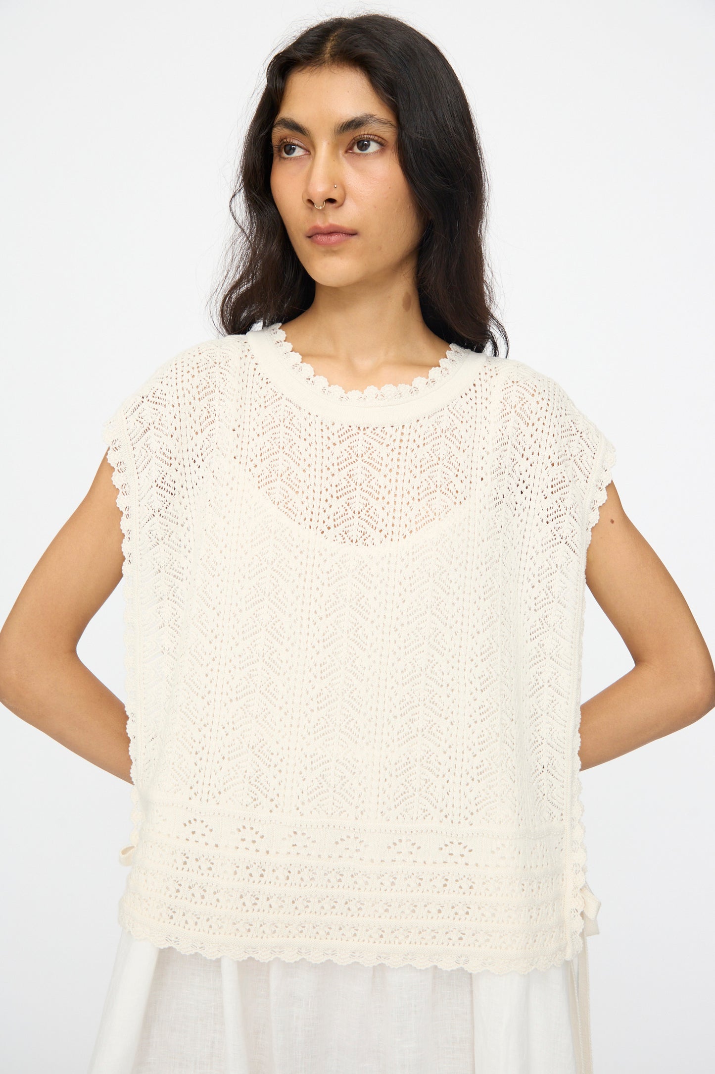 A woman in the nest Robe Openwork Lace Knit Vest in Off White, worn over a white dress, stands against a plain white background.