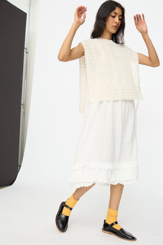 A person wearing the nest Robe Openwork Lace Knit Vest in Off White, a cotton linen blend skirt, black shoes, and yellow socks stands with arms raised against a plain studio background.