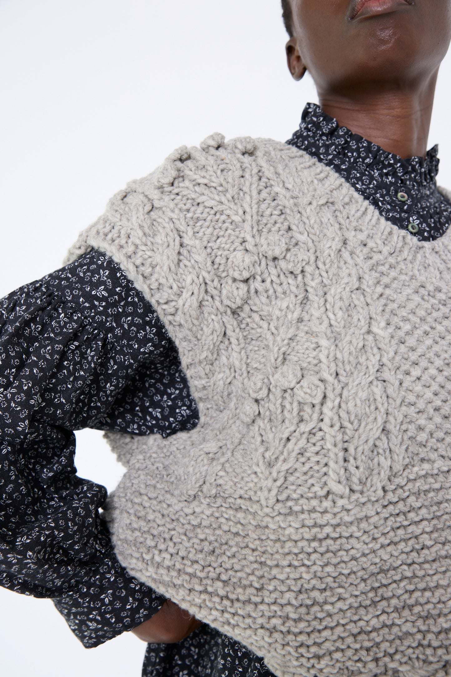 Close-up of a woman wearing nest Robe's Peruvian Wool Bobble Knit Two-Way Vest in Beige over a patterned long-sleeve shirt against a white background.