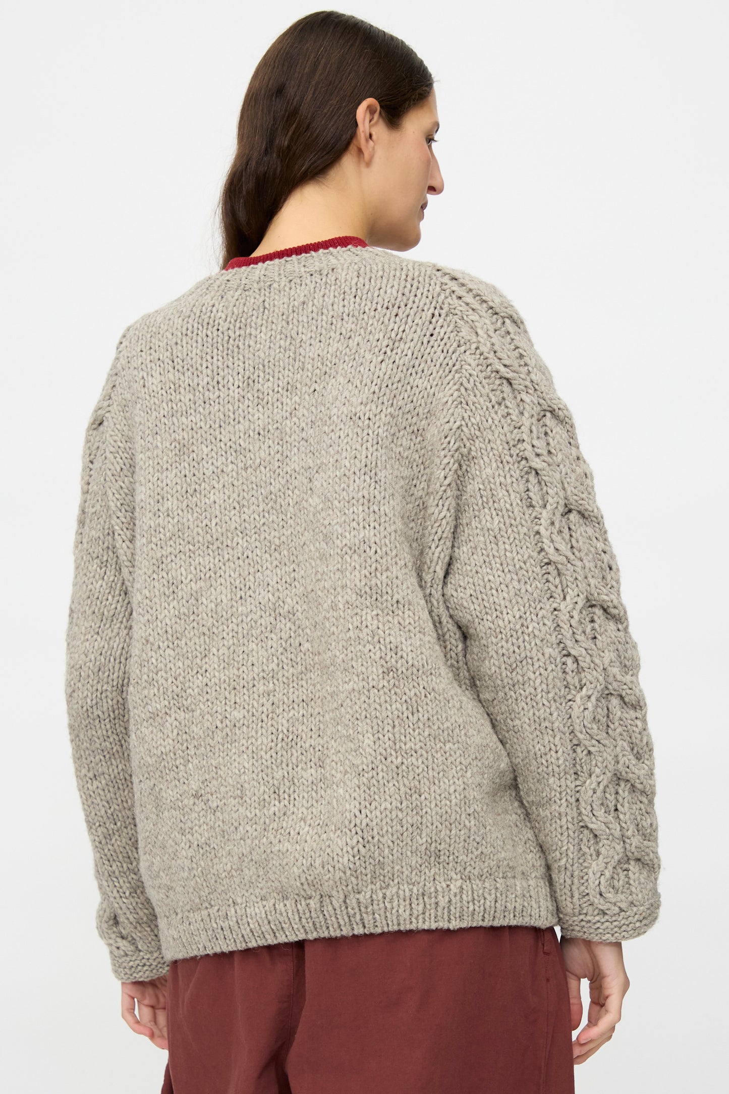 A person is seen from the back against a plain background, wearing nest Robe’s Peruvian Wool Cable Sleeve Knit Cardigan in Beige, styled with a maroon skirt.