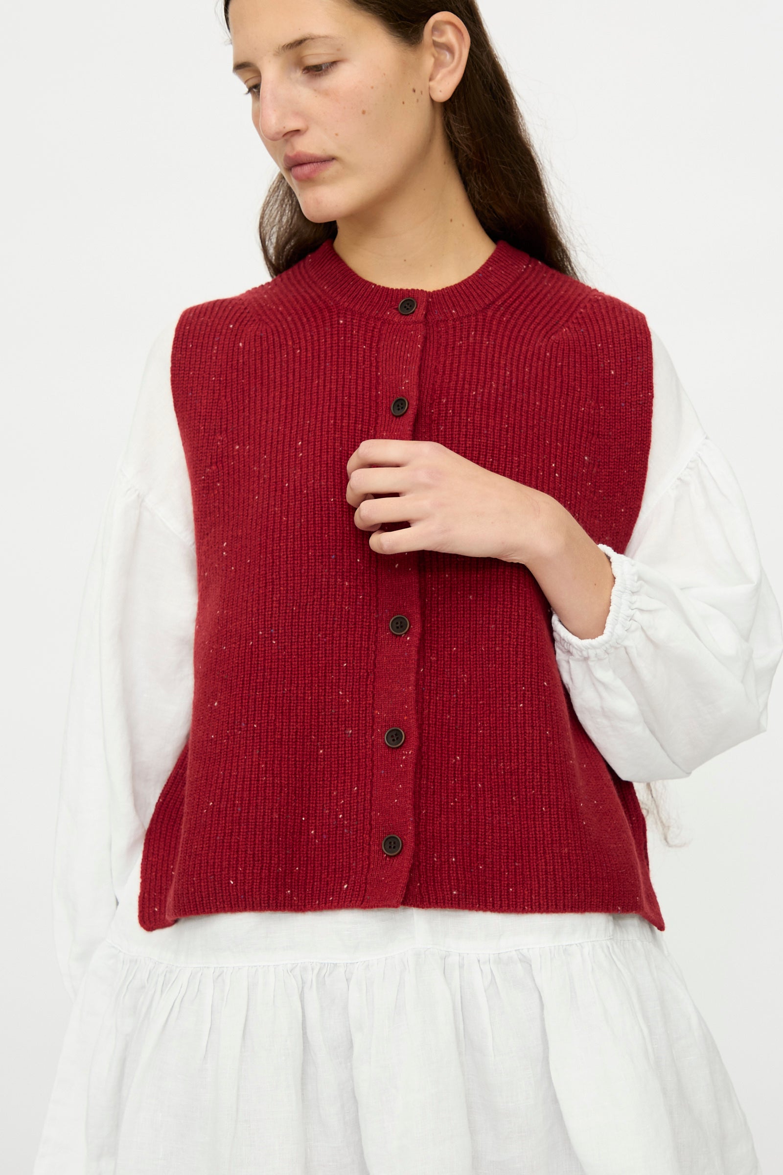 A woman wears a white long-sleeve dress and the nest Robe Rib Knit Buttoned Vest in Wine, standing against a plain light background.