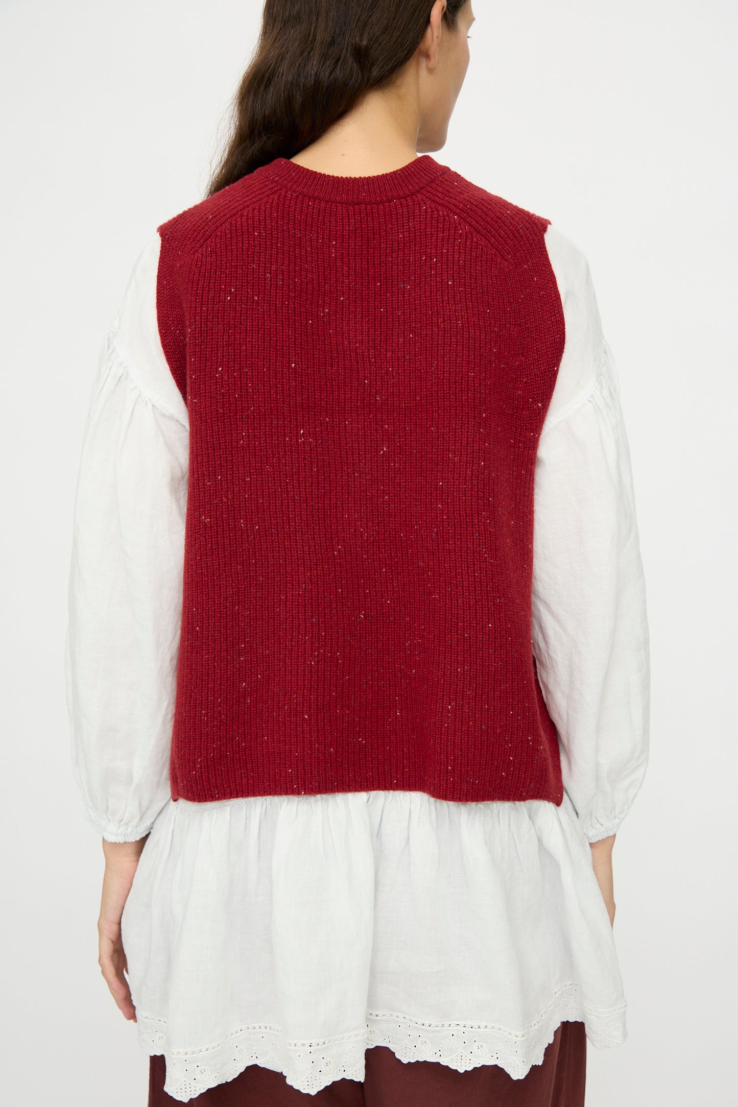 A person with long brown hair, seen from behind, wears the nest Robe Rib Knit Buttoned Vest in Wine over a loose-fitting white blouse.