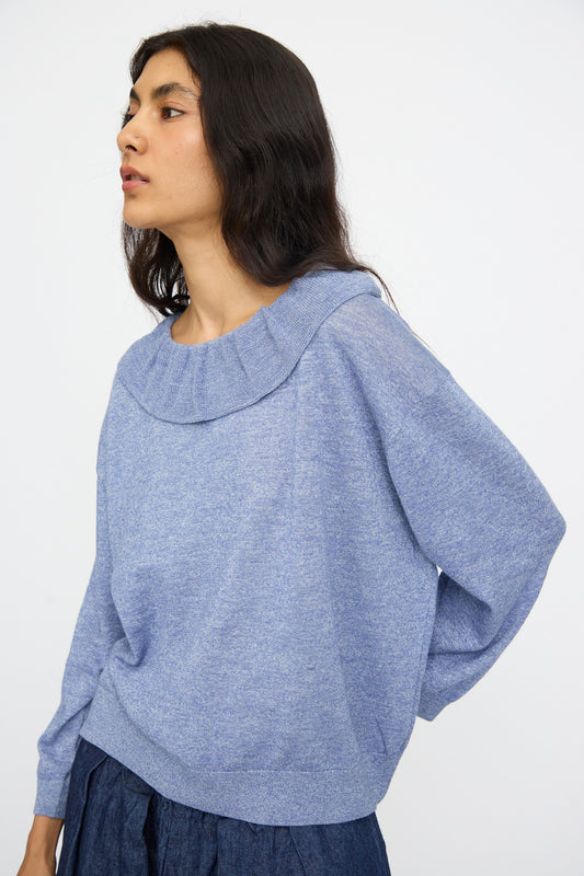 A person with long dark hair wears the nest Robe Ruffle Collar Knit Pullover in Blue, paired with a dark blue skirt, and stands against a plain light background. This pullover is thoughtfully made in Japan.