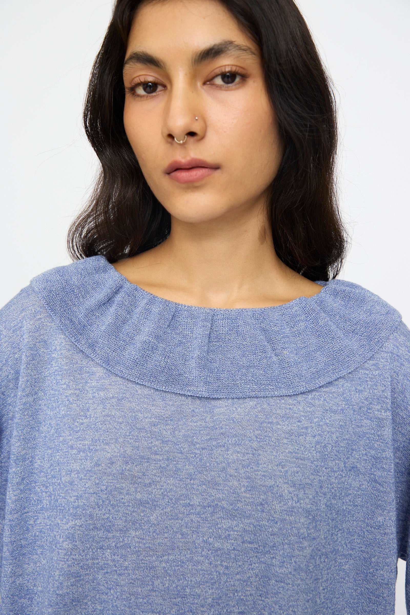 A person with long dark hair and a nose ring is wearing the nest Robe Ruffle Collar Knit Pullover in Blue, facing forward against a plain background.