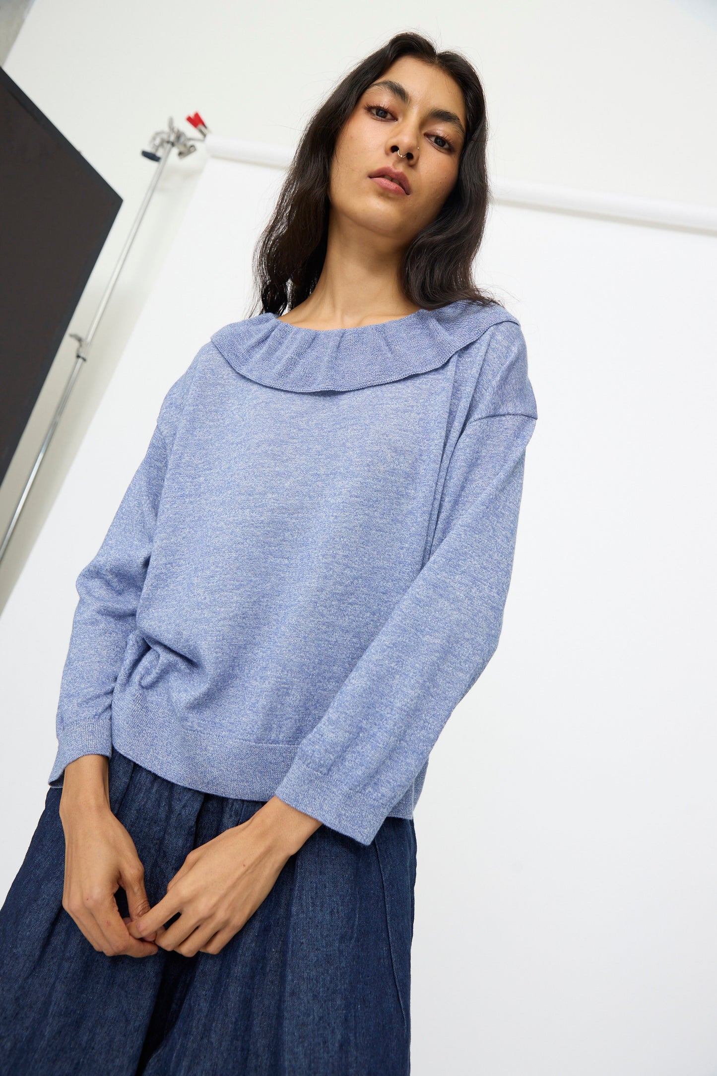 A woman wears the nest Robe Ruffle Collar Knit Pullover in blue with a navy skirt, standing against a plain white background. Made in Japan.