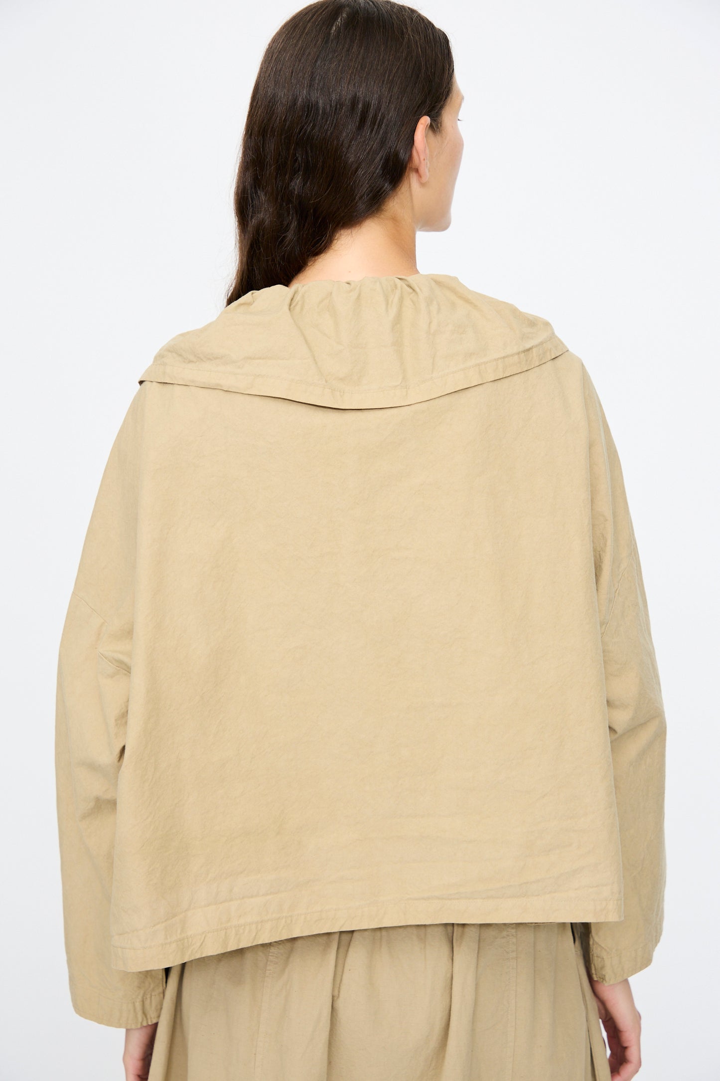 A person with long brown hair, seen from behind, wears the nest Robe Super Water-Repellent Supima Cotton Leaf Collar Jacket in beige and a matching skirt.