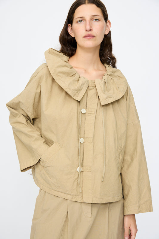 A person wears the nest Robe Super Water-Repellent Supima Cotton Leaf Collar Jacket in Beige, featuring a loose, boxy fit and large buttons, paired with matching beige pants, standing against a plain light background.