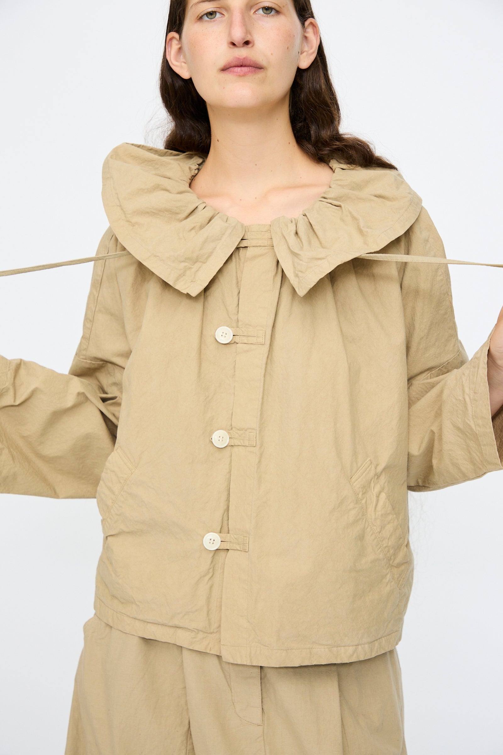 A person wears the nest Robe Super Water-Repellent Supima Cotton Leaf Collar Jacket in Beige with matching pants, holding out the collar ties against a plain white background.