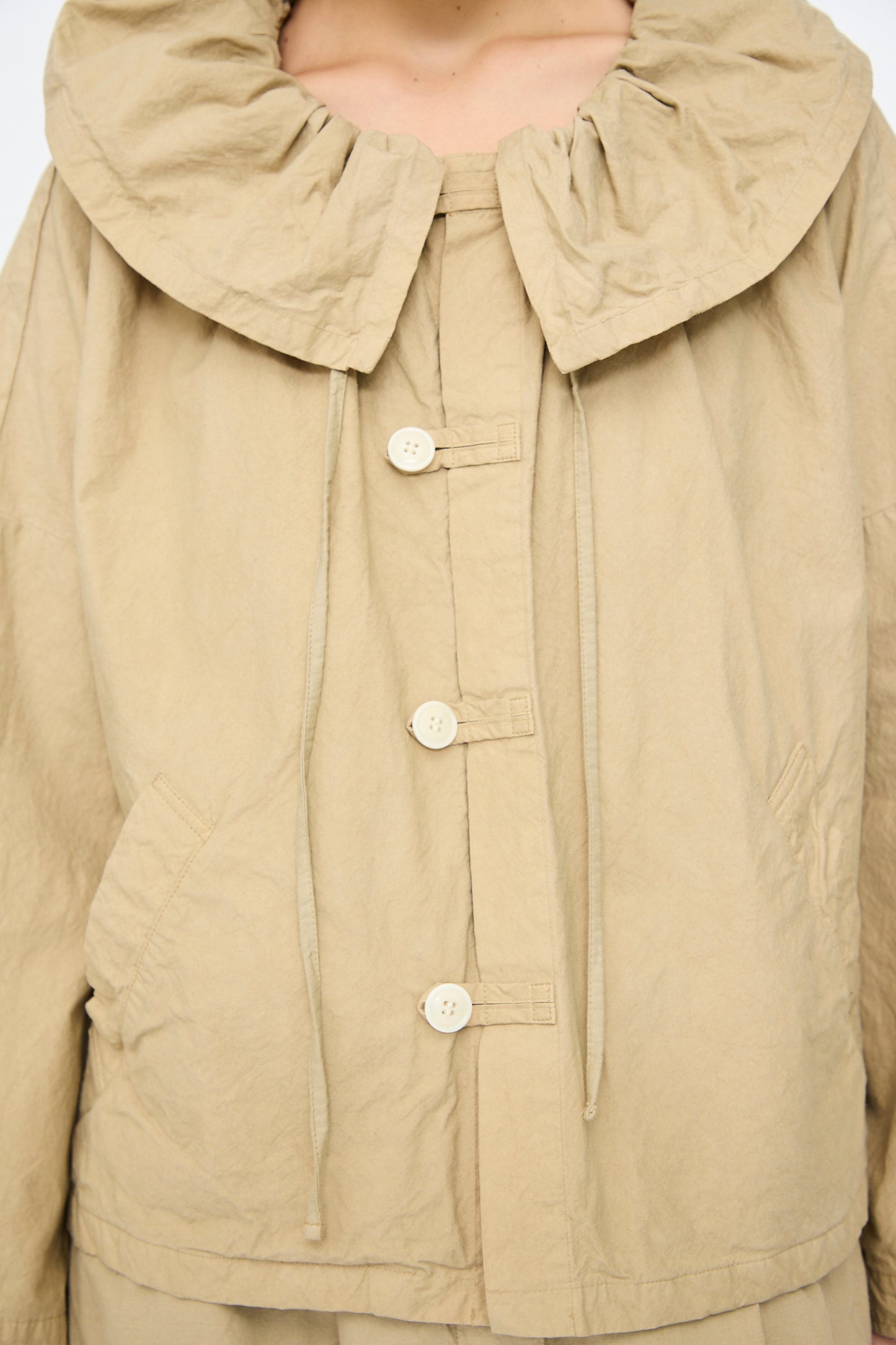 A person wearing the beige Super Water-Repellent Supima Cotton Leaf Collar Jacket by nest Robe, featuring a wide gathered collar, two front pockets, button-up design, and boxy fit.
