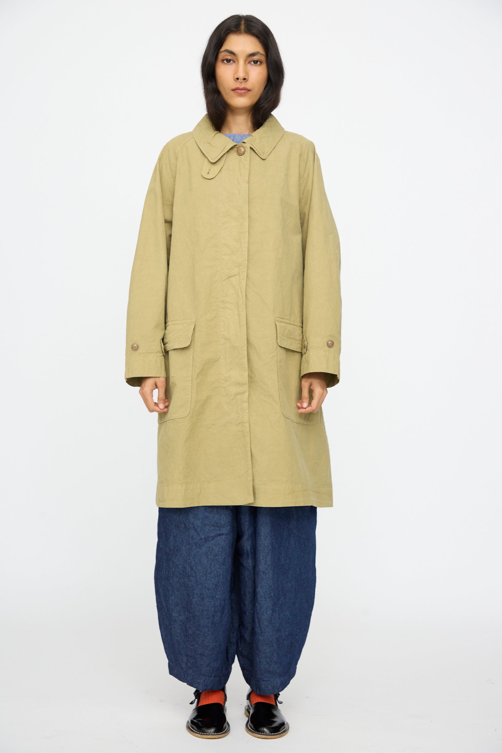 A person faces forward wearing the nest Robe Supima Cotton Topcoat in Green over wide blue pants and black shoes, set against a plain white background.