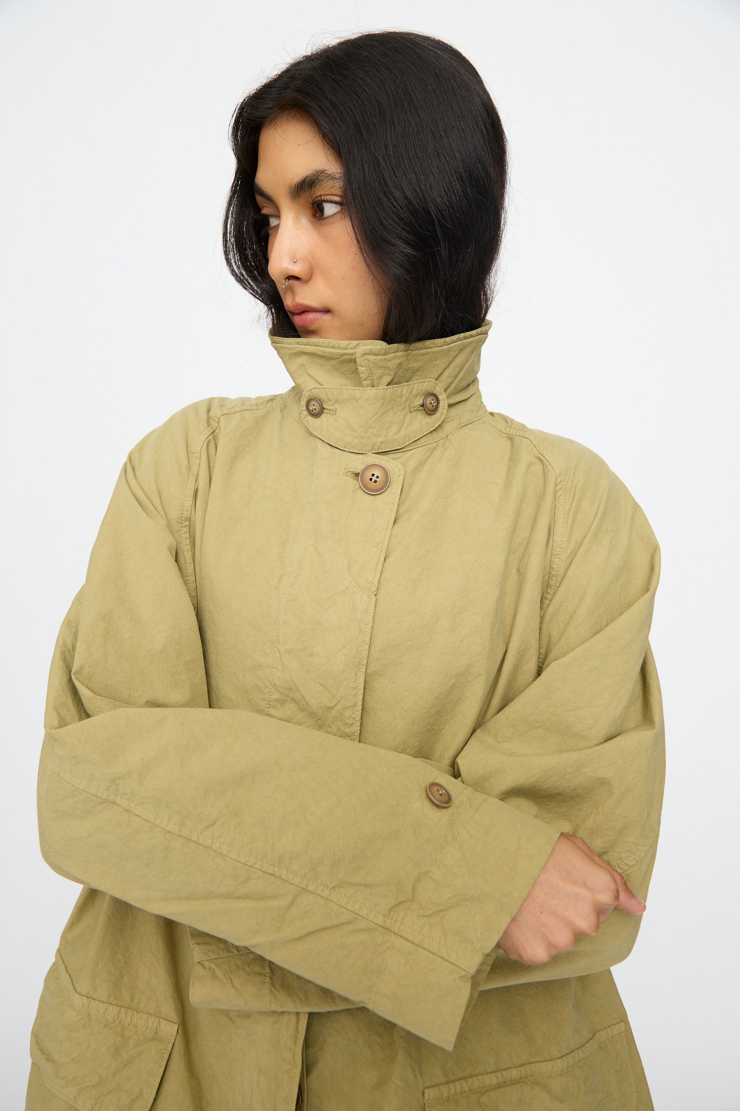 A person wears the nest Robe Supima Cotton Topcoat in green, a loose-fitting style with large buttons and a high collar, looking to the side against a plain background.