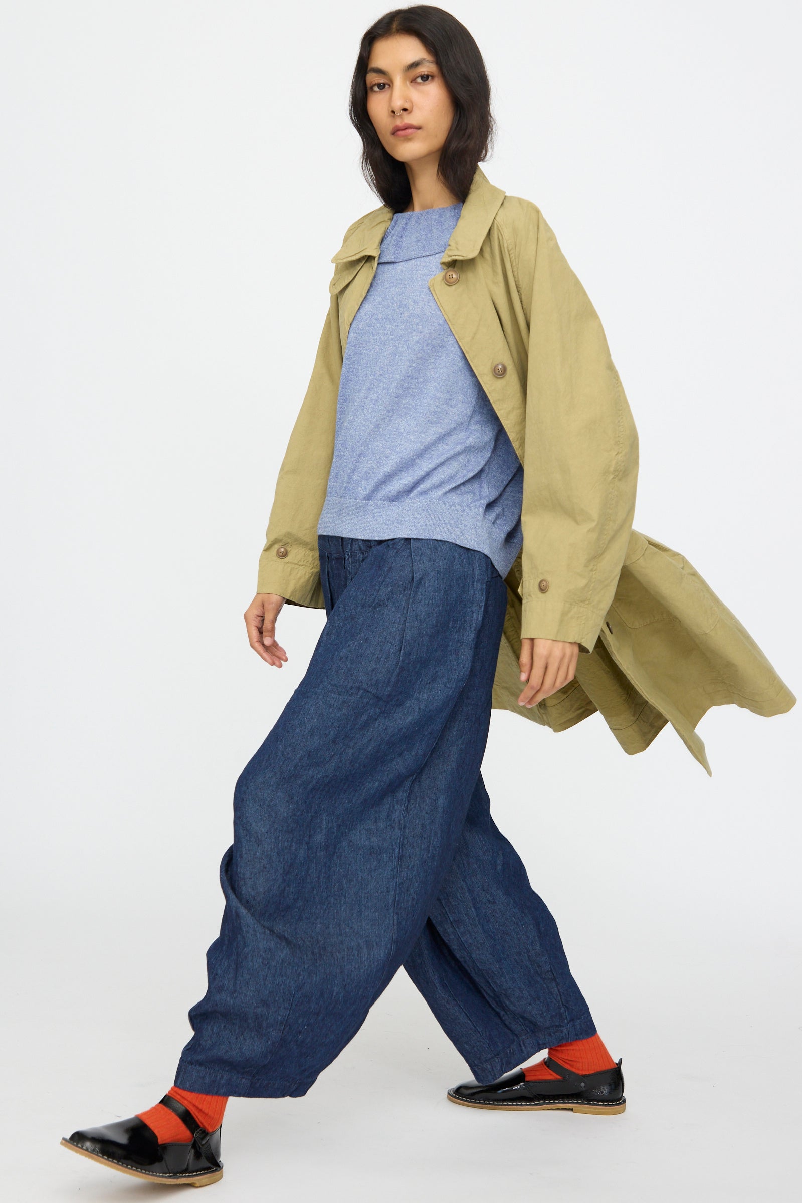 A person wears the nest Robe Supima Cotton Topcoat in Green over a blue sweater, styled with wide-leg denim pants, red socks, and black shoes—posing against a plain white background. The outfit channels classic Japanese topcoat style.