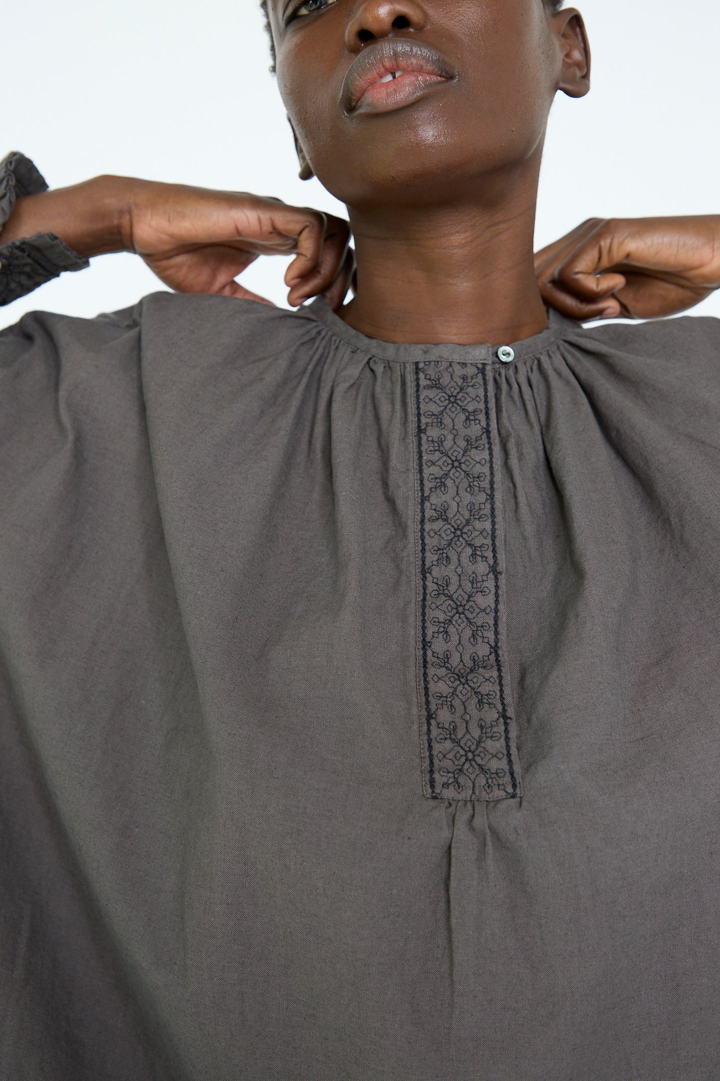 A close up of a woman adjusting the collar of nest Robe's UpcycleLino Cotton Linen Embroidered Tunic in Grey. 